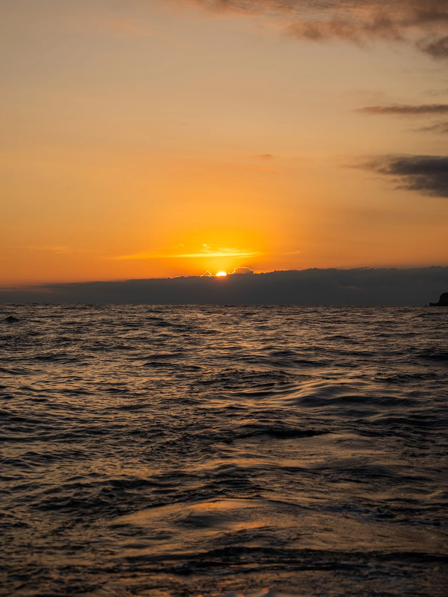 Atardecer sobre el océano con cielo nublado y reflejos dorados en las aguas.