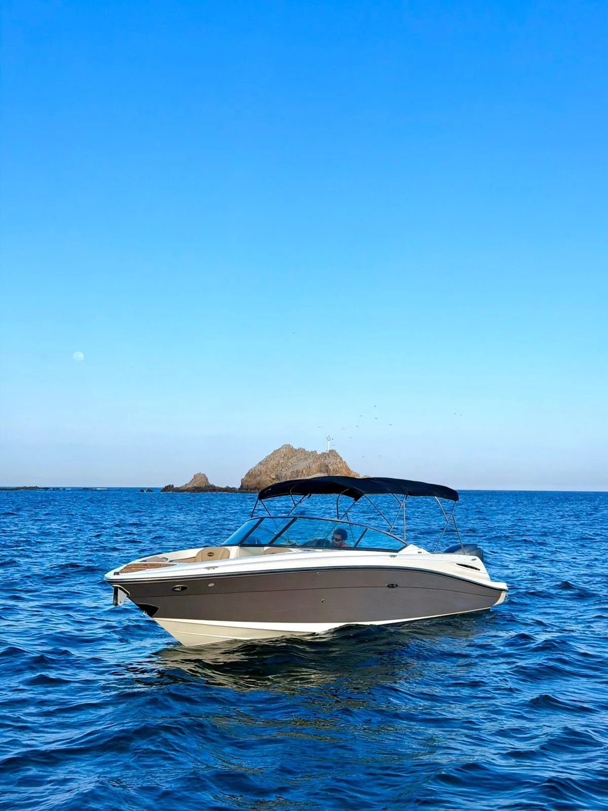 Bote de lujo navegando en el mar con una isla en el fondo bajo un cielo despejado