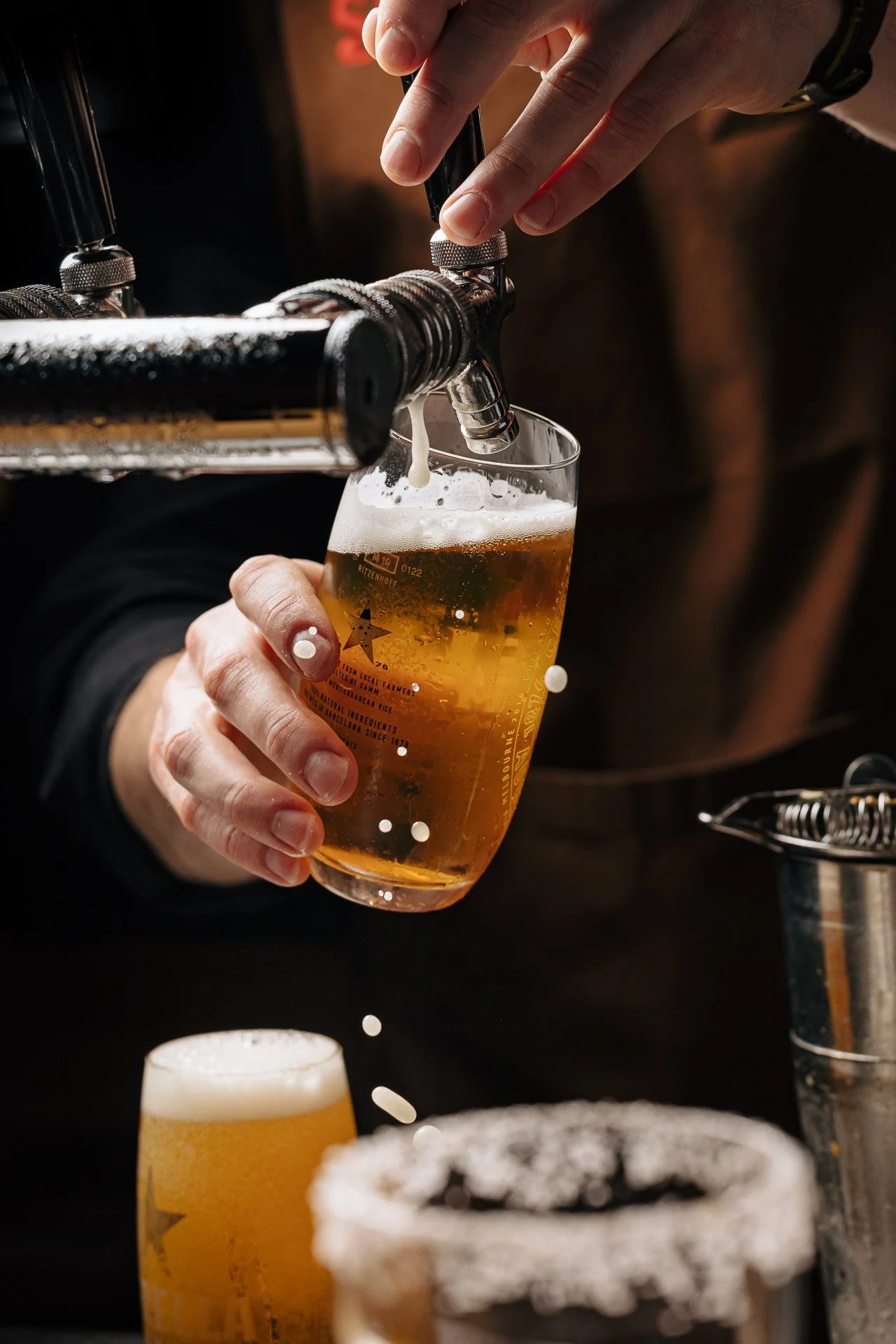 A person pouring beer from a tap into a glass, with two other glasses of beer in the foreground.
