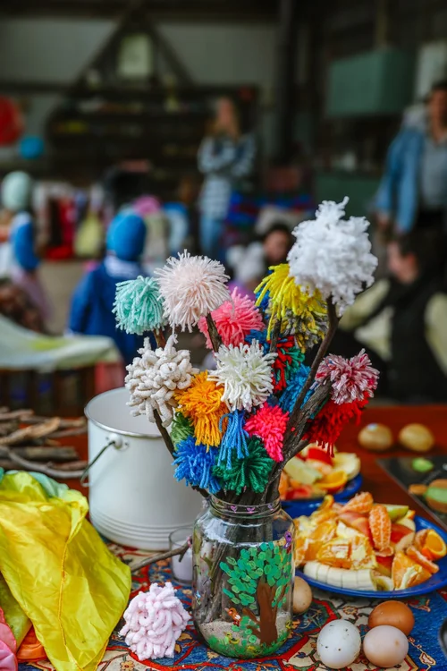 Colourful yarn pom pom bouquet displayed with fresh fruit and eggs on a market table