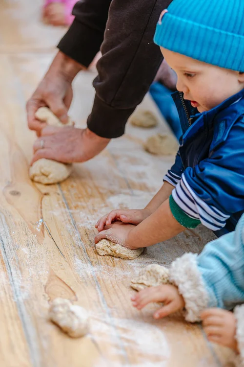 A child kneading bread dough on a floured table with an adult