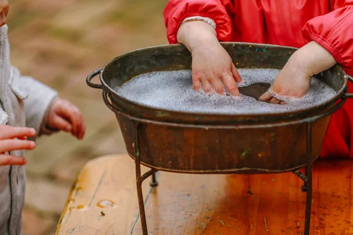 Child washing hands in a large metal basin outdoors