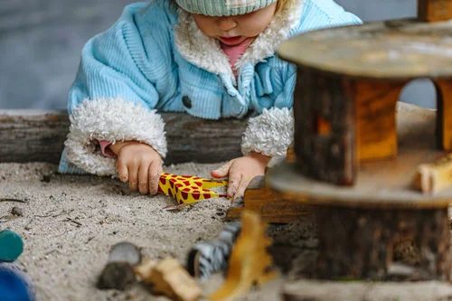 Toddler playing with a wooden toy on a tree stump table outdoors
