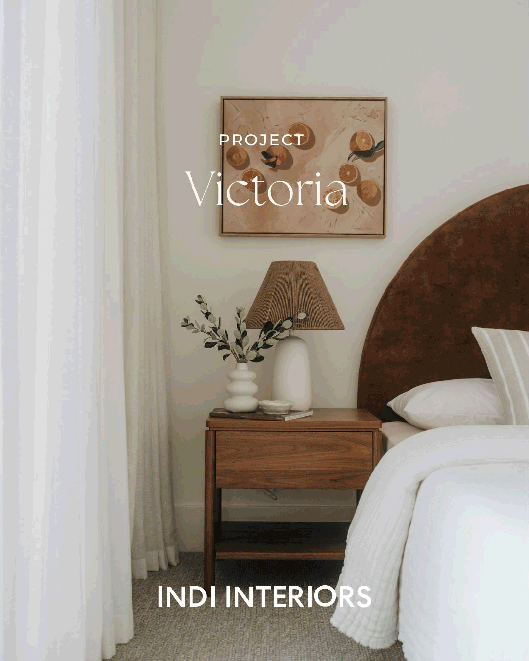 Decorative bedroom scene with a wooden nightstand, a white ceramic vase with green leaves, a table lamp with a beige shade, and a framed abstract art hanging on the wall.