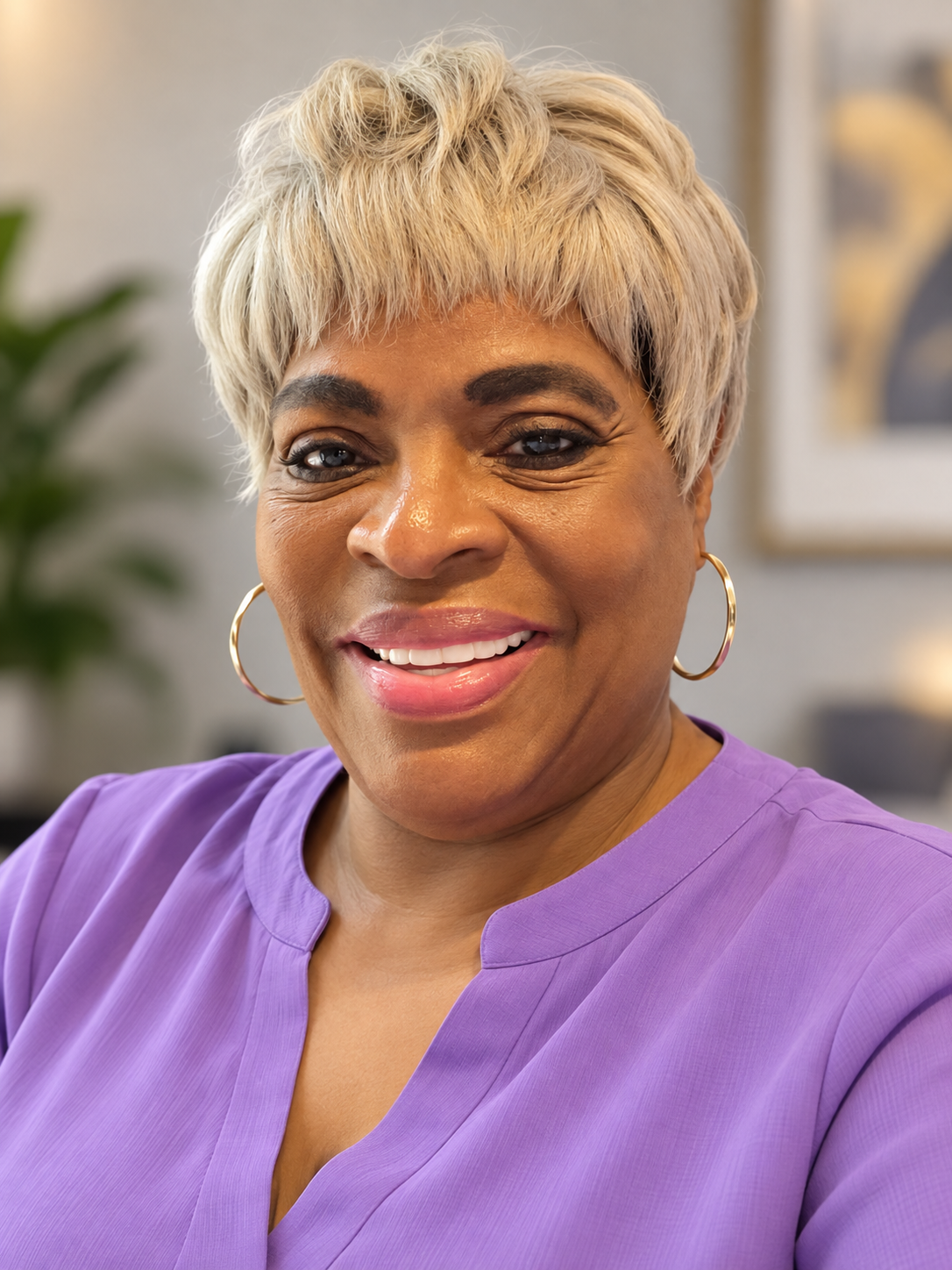 Close-up of a smiling African American woman with short blonde hair, wearing gold hoop earrings and a purple top.
