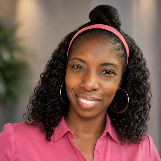 A young woman with curly black hair, wearing a pink headband, hoop earrings, and a pink collared shirt, smiling at the camera.