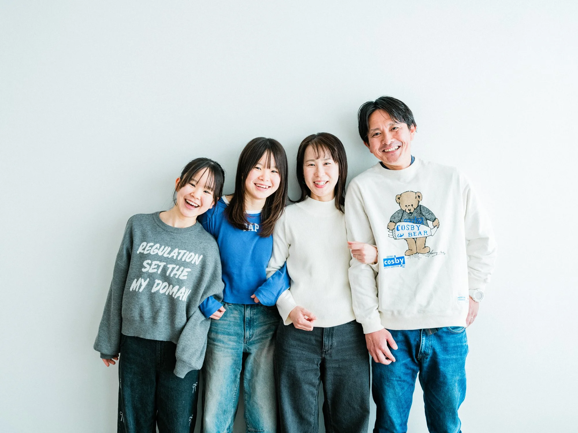 笑顔の家族4人が壁の前に立ち、並んでいる写真です。
