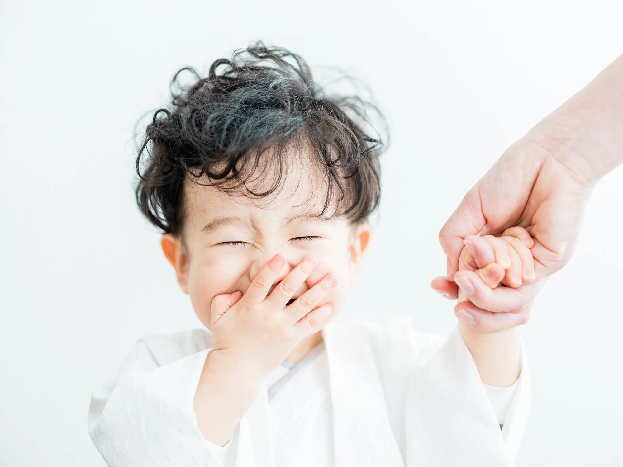 子供が笑顔で顔を手で隠し、お母さんの手を握っている写真。
