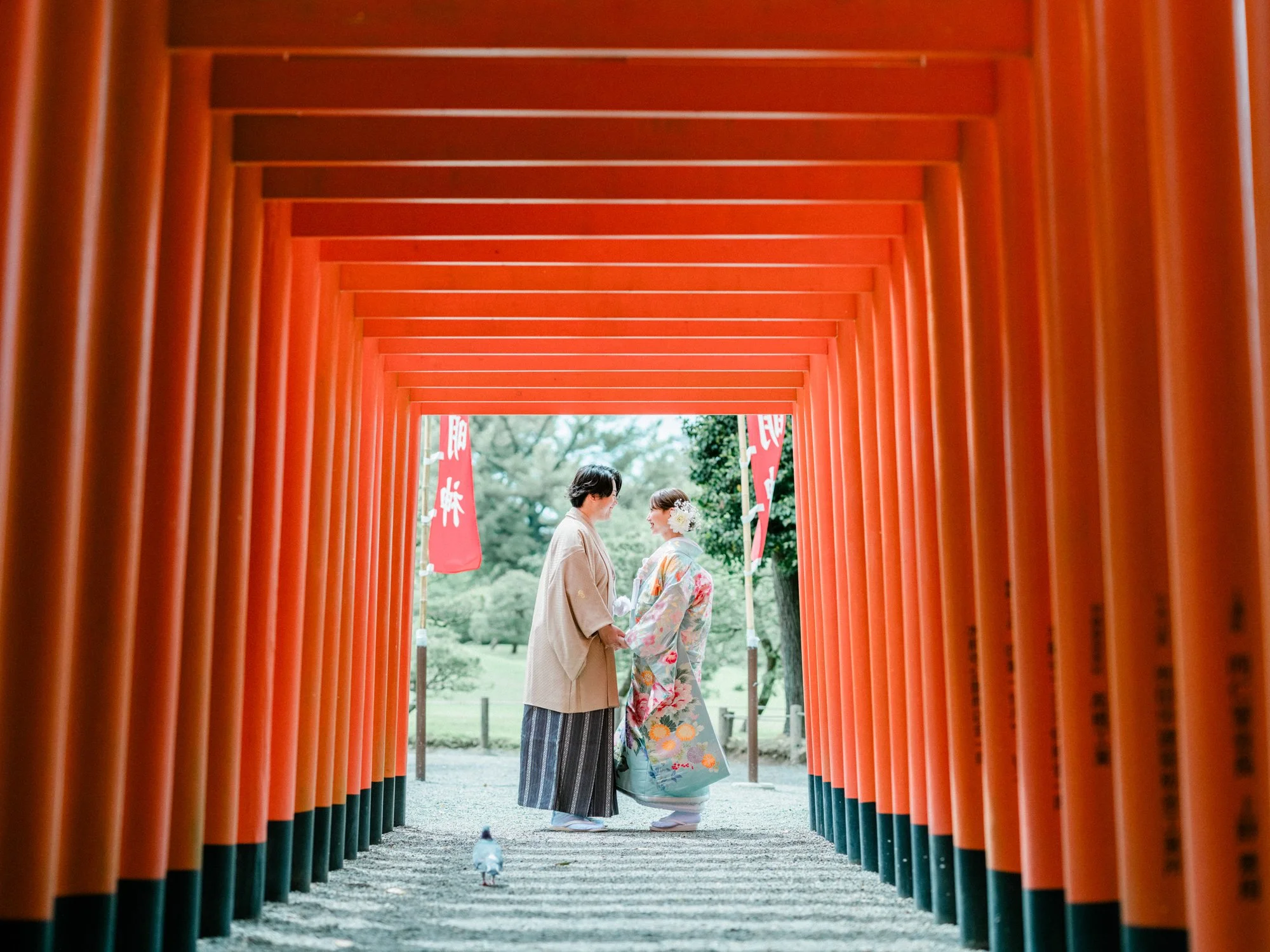 二人の女性が熊本の神社で着物を着て話している。朱色の鳥居の間を歩いている。
