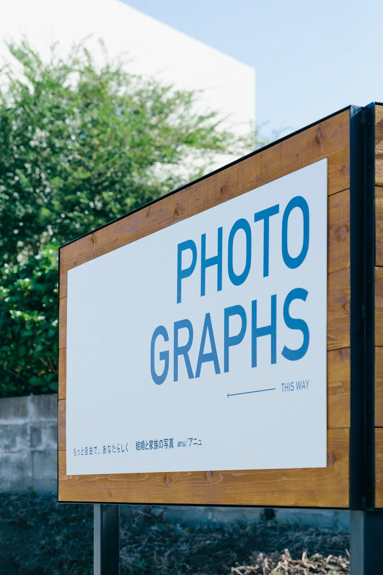 木製の看板に『PHOTOGRAPHS』と書かれたサイン。背景には木と青空が見える。