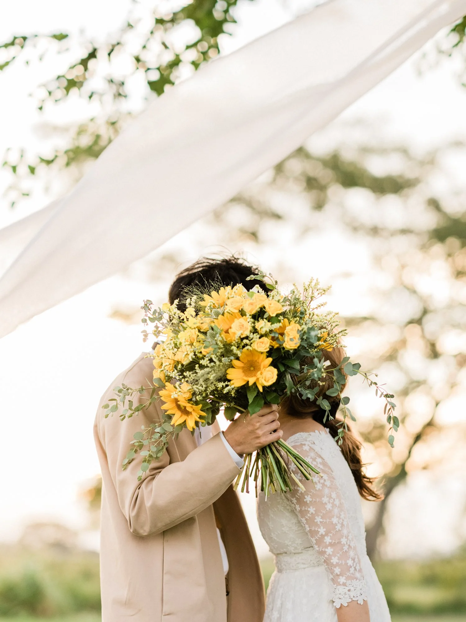 結婚式を挙げている新郎新婦が、ブーケの花束で顔を隠している。