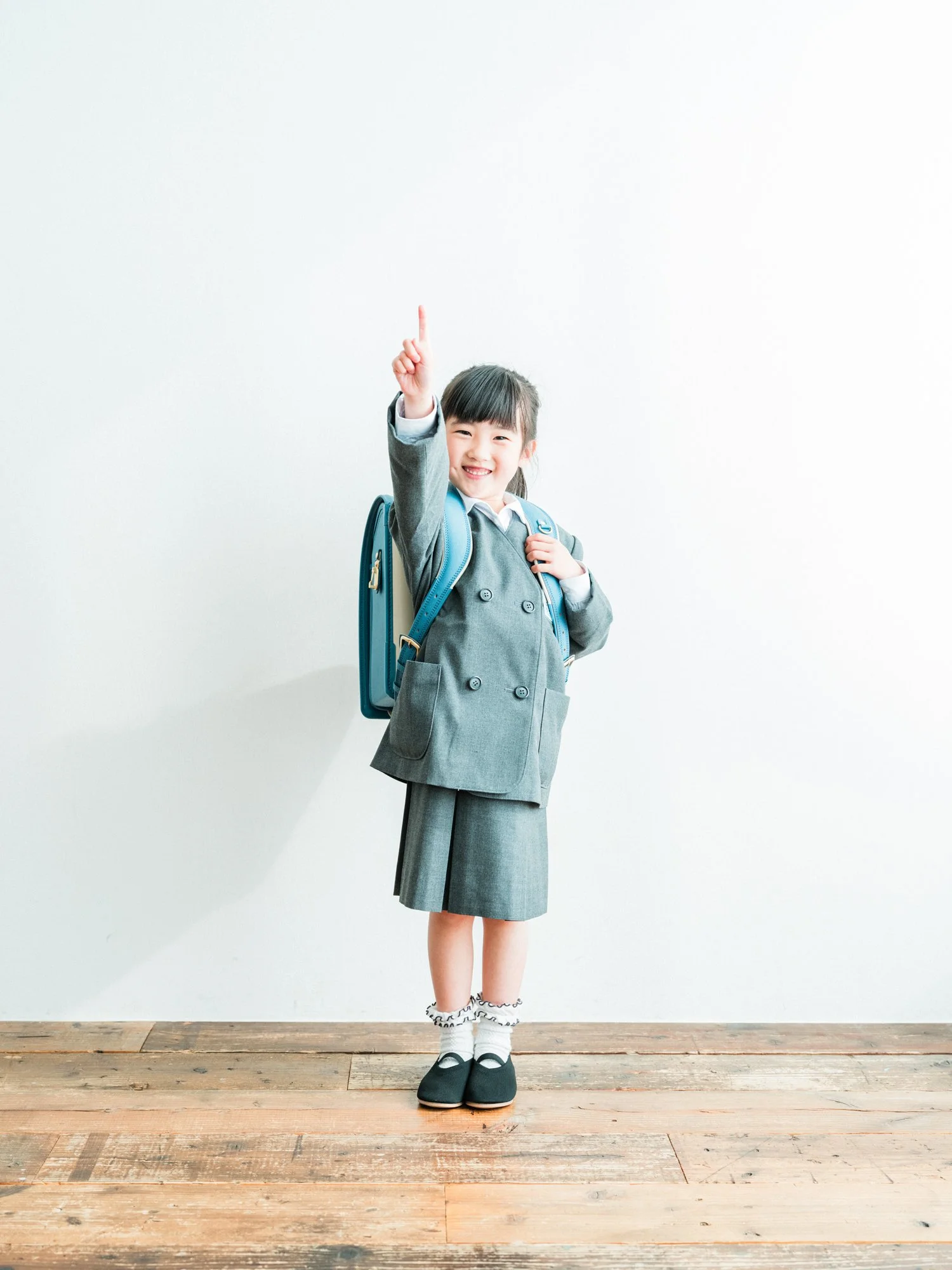 制服を着た女の子が笑顔で立ち、片手を挙げている。