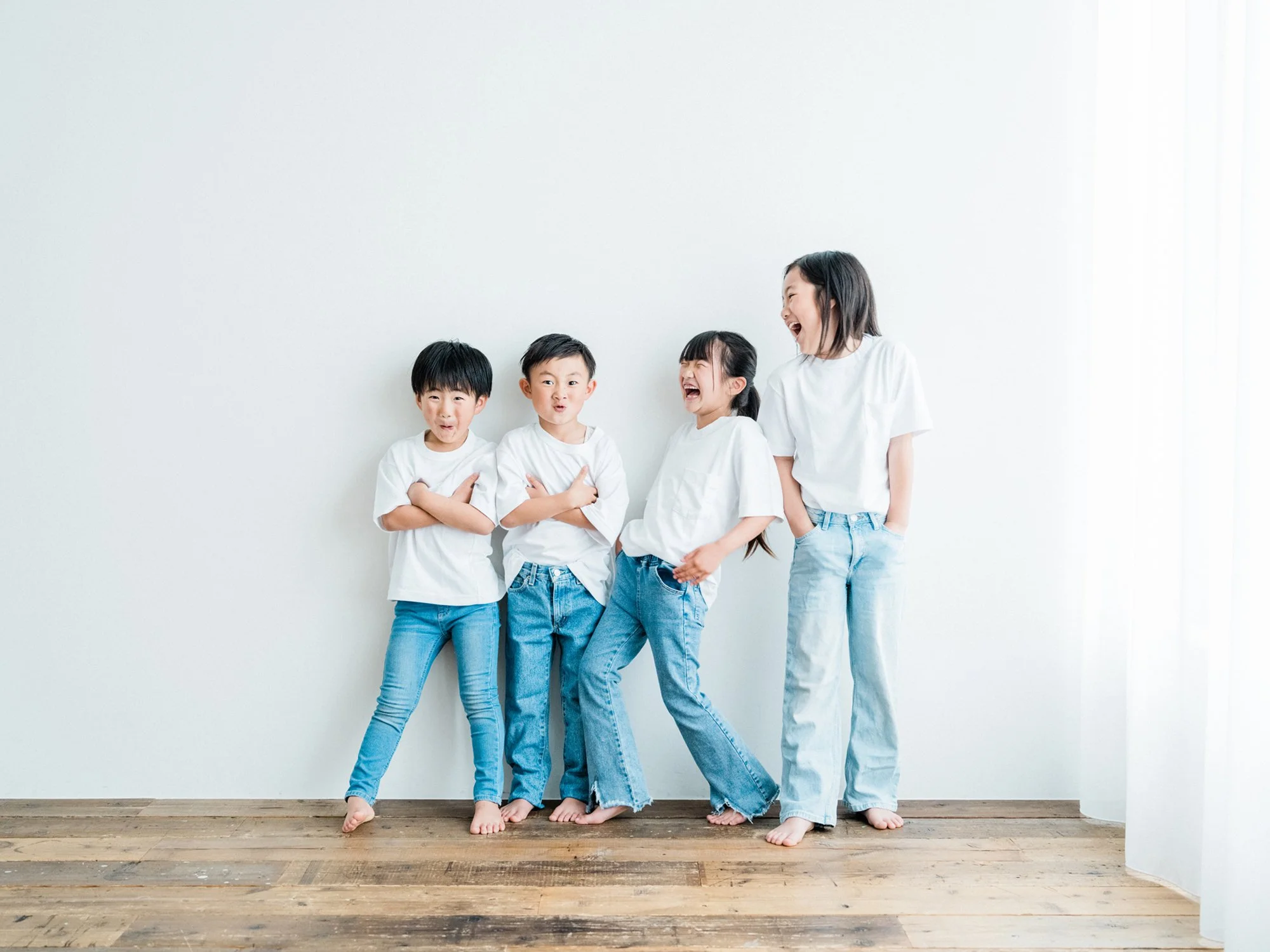 白いTシャツとジーンズを着た子供と女性が笑いながらお互いに近づいて、白い壁の前でポーズをとっている様子