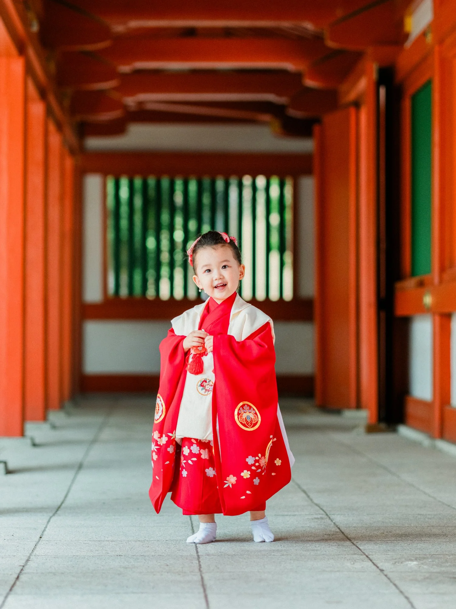 伝統的な赤と白の着物を着ている子供の女の子、神社の門の前に立っている。