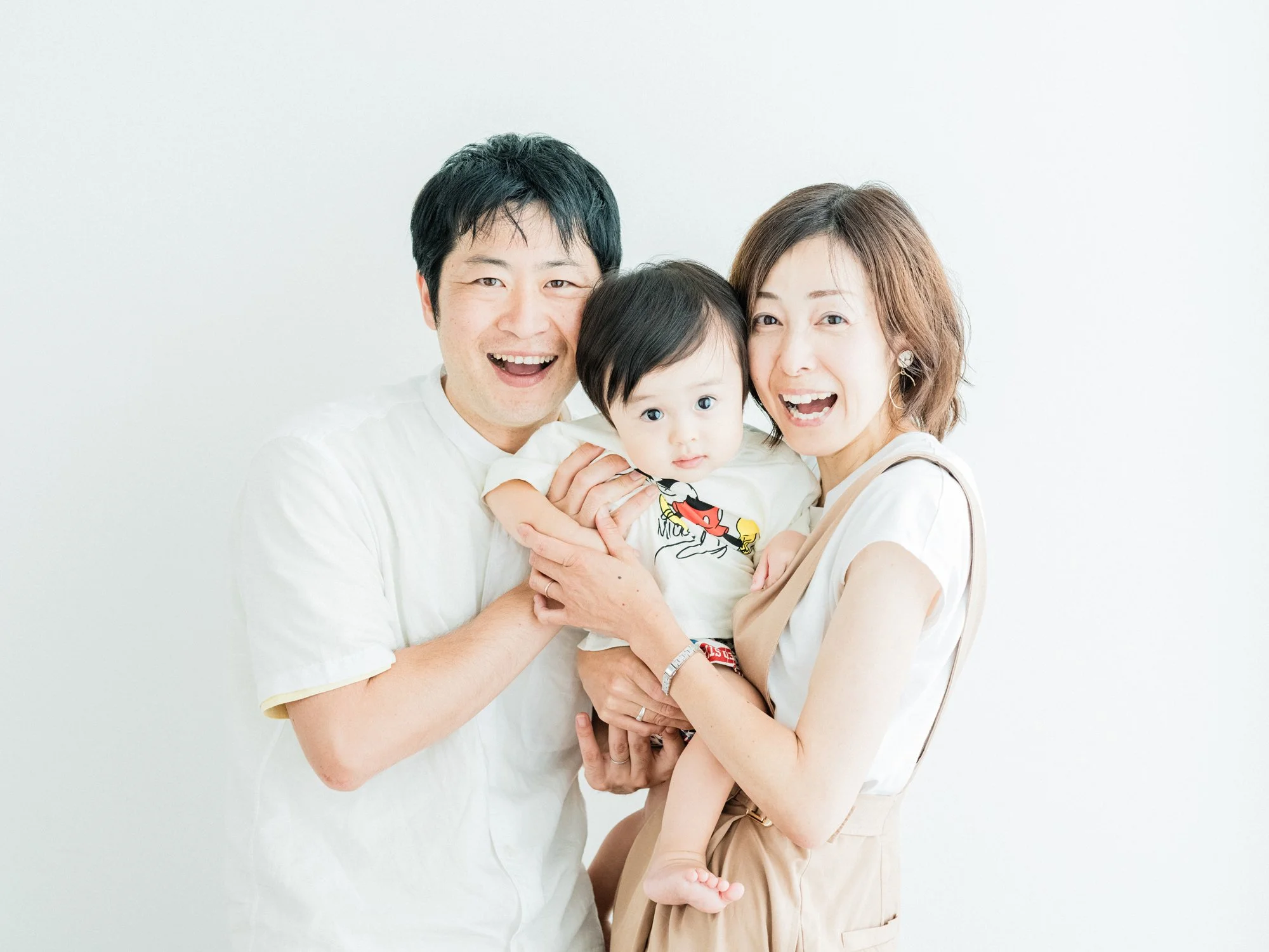 白い背景の前で笑顔の家族、両親と幼い男の子を抱きしめ合っている。