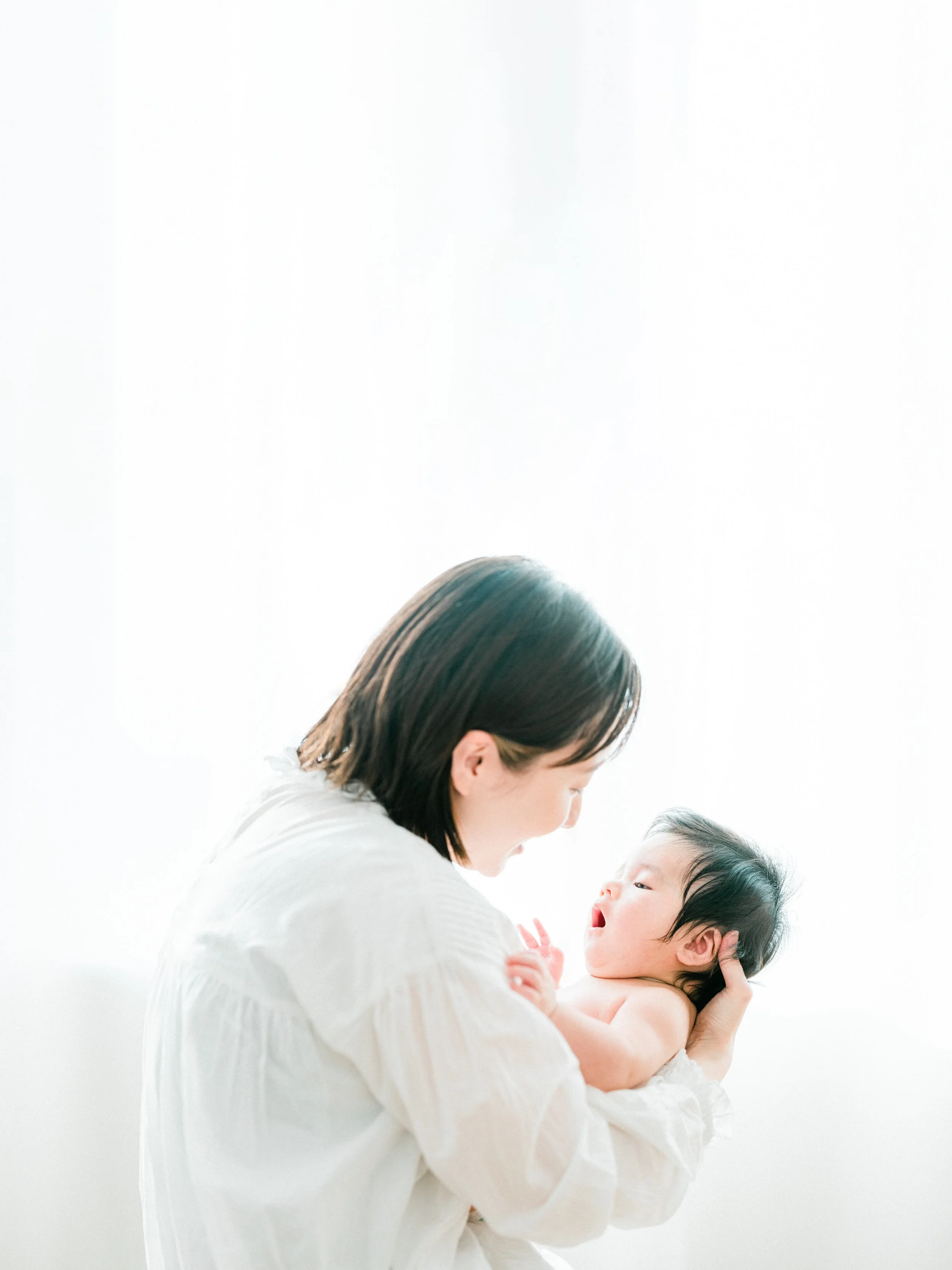 白い背景の前で母親が赤ちゃんを抱きしめる写真