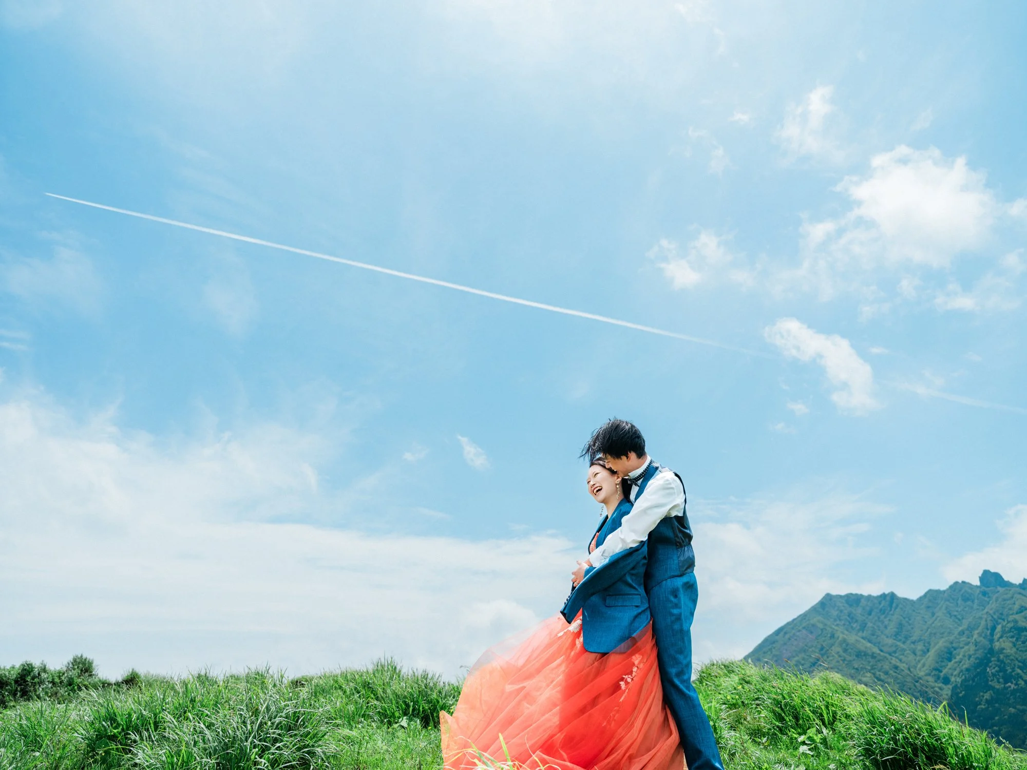 結婚式の前撮りで新郎新婦が青空の下で抱き合っている。