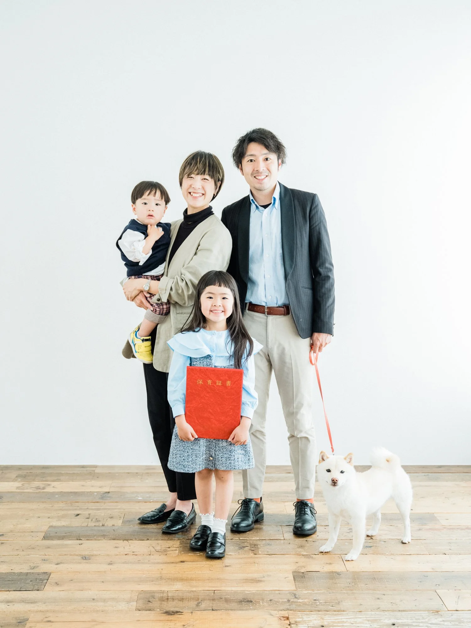 家族とワンちゃんの写真。4人の家族と白い犬が白い背景の前に立っている。