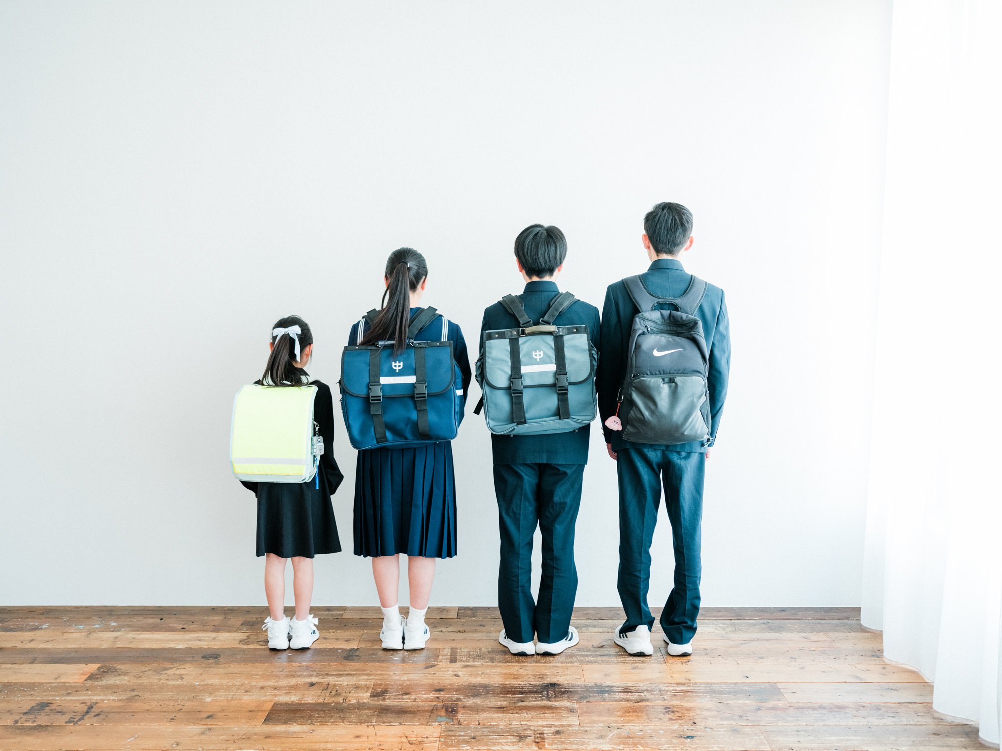 制服を着た四人の学生が壁に向かって立っている写真。