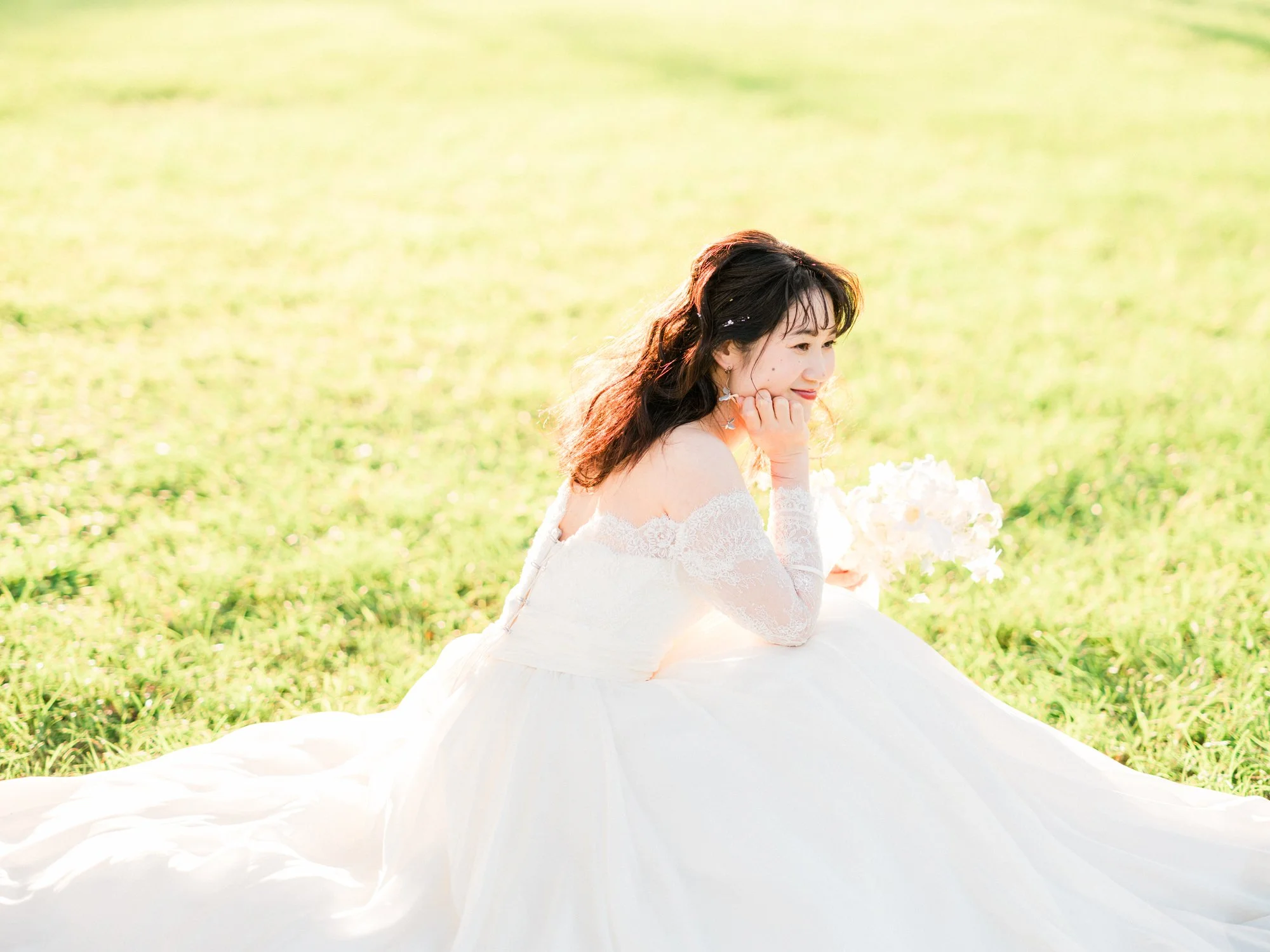 白いドレスを着た若い女性が草原に座って微笑んでいる。