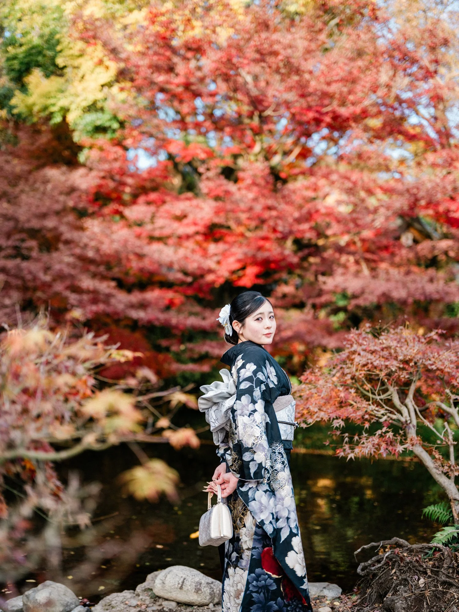 紅葉の木の下で振袖を着た女性が振り返っている。
