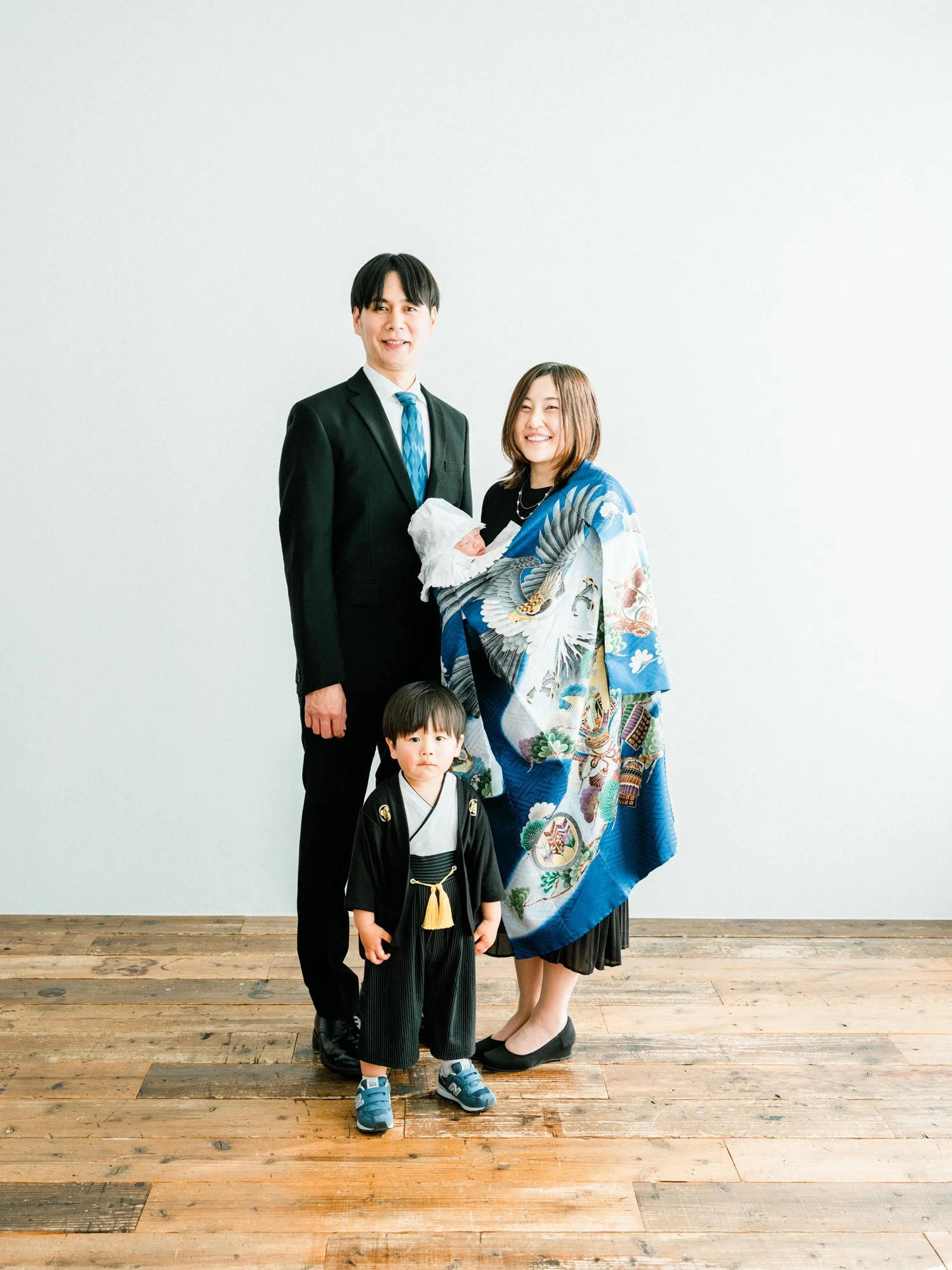 お宮参りの記念写真。家族が木製の床の前で写真を撮っている。赤ちゃんを抱いている女性と、男の子が前に立ち、父と母が後ろに立っている。