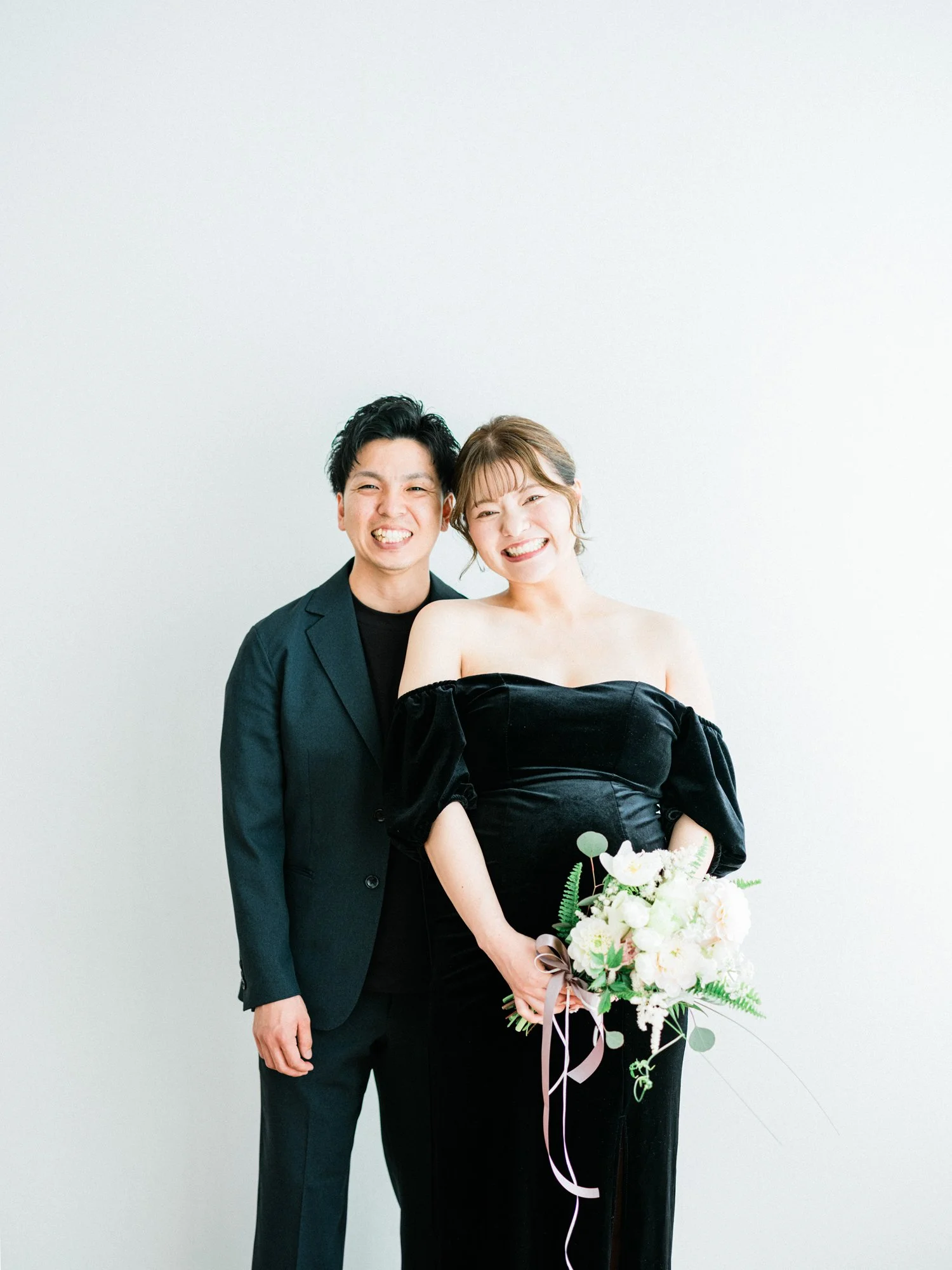 笑顔の男女のマタニティ写真。女性は花束を持ち、ドレス姿。
