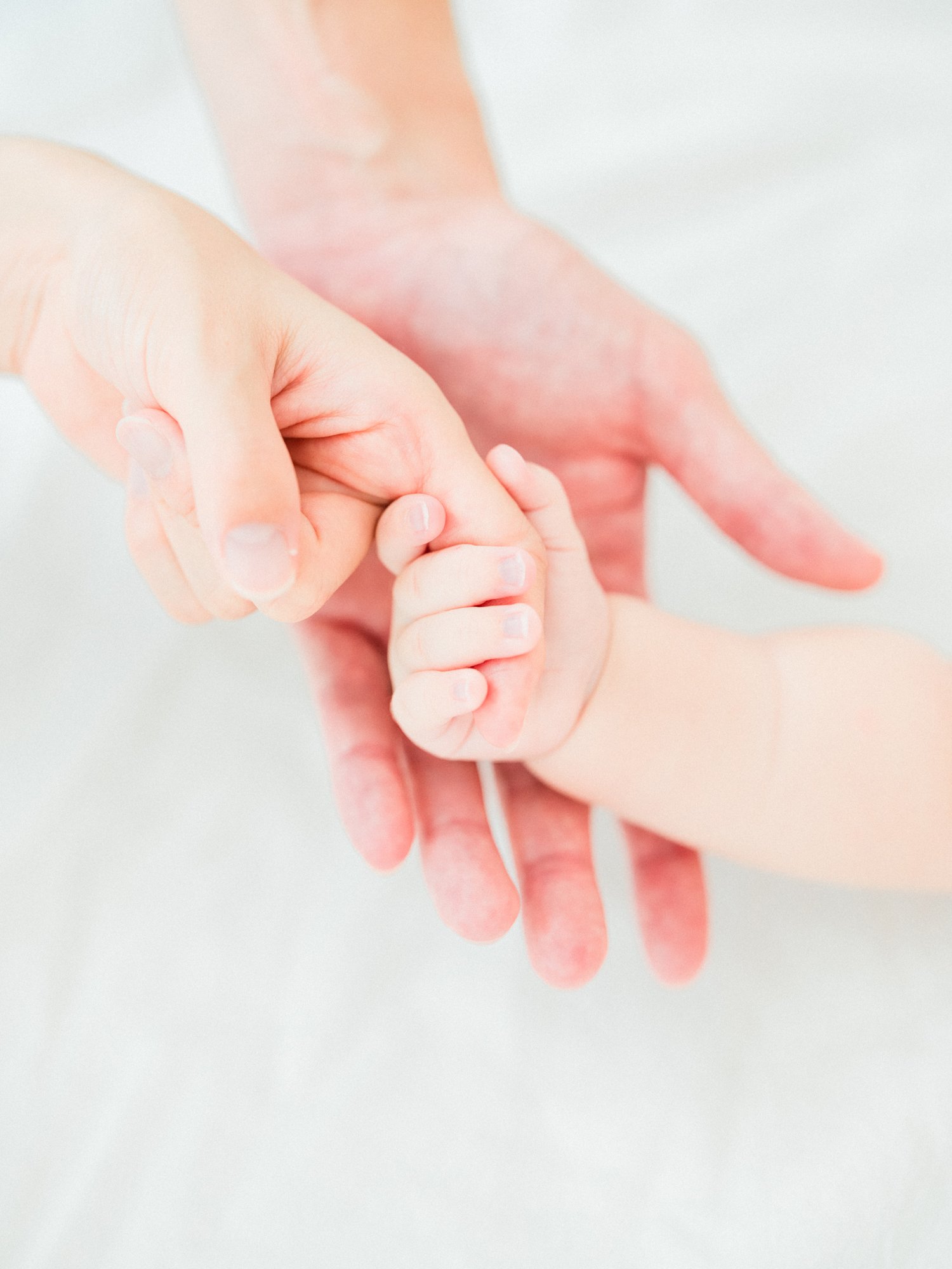 赤ちゃんの小さな手を優しく握るパパとママの手。