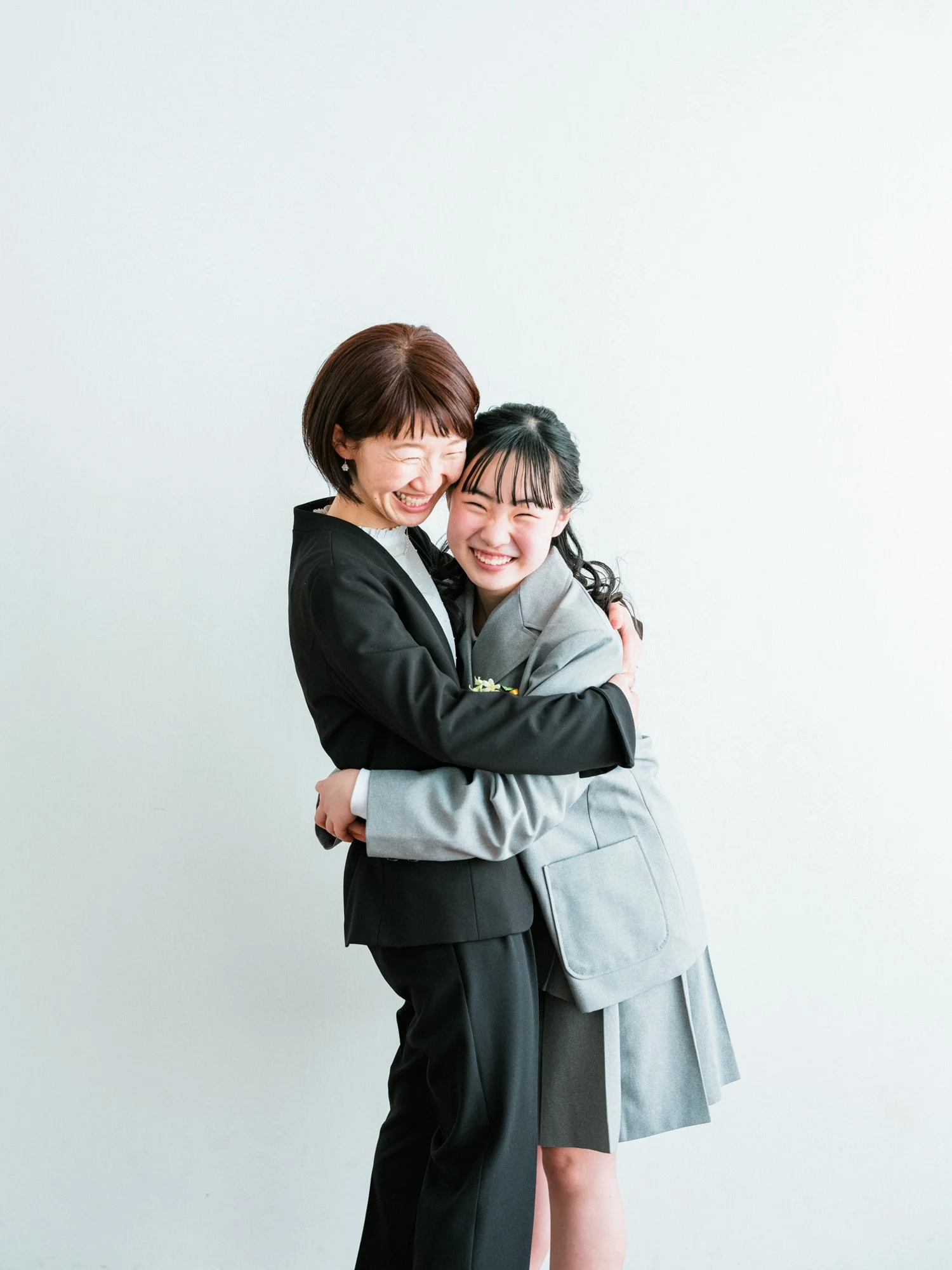 笑顔の女性と女の子がハグしている写真。背景は白の壁。