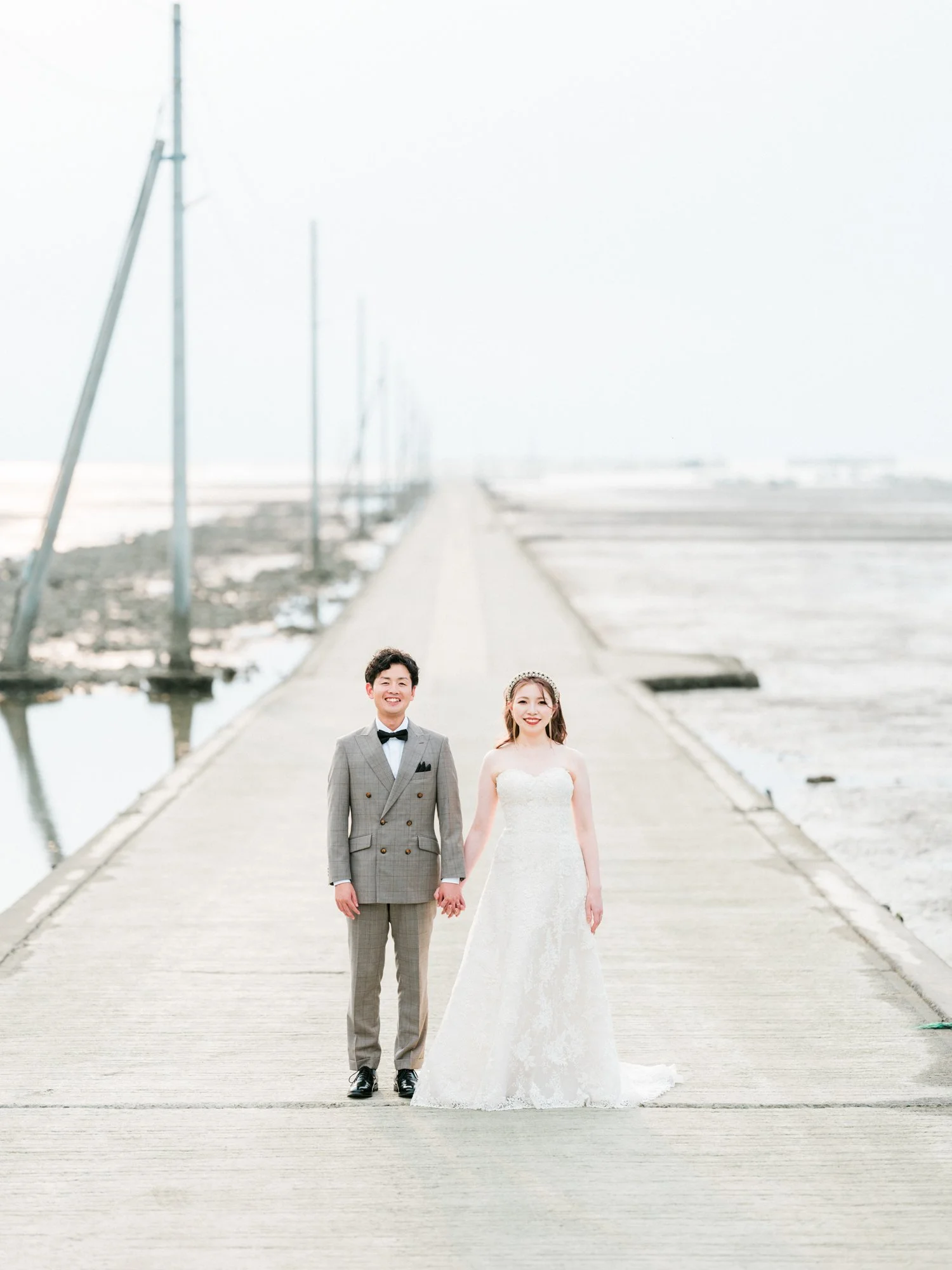 結婚式をしているカップルが海辺の桟橋の上で手をつないでいます。背景は空と海です。