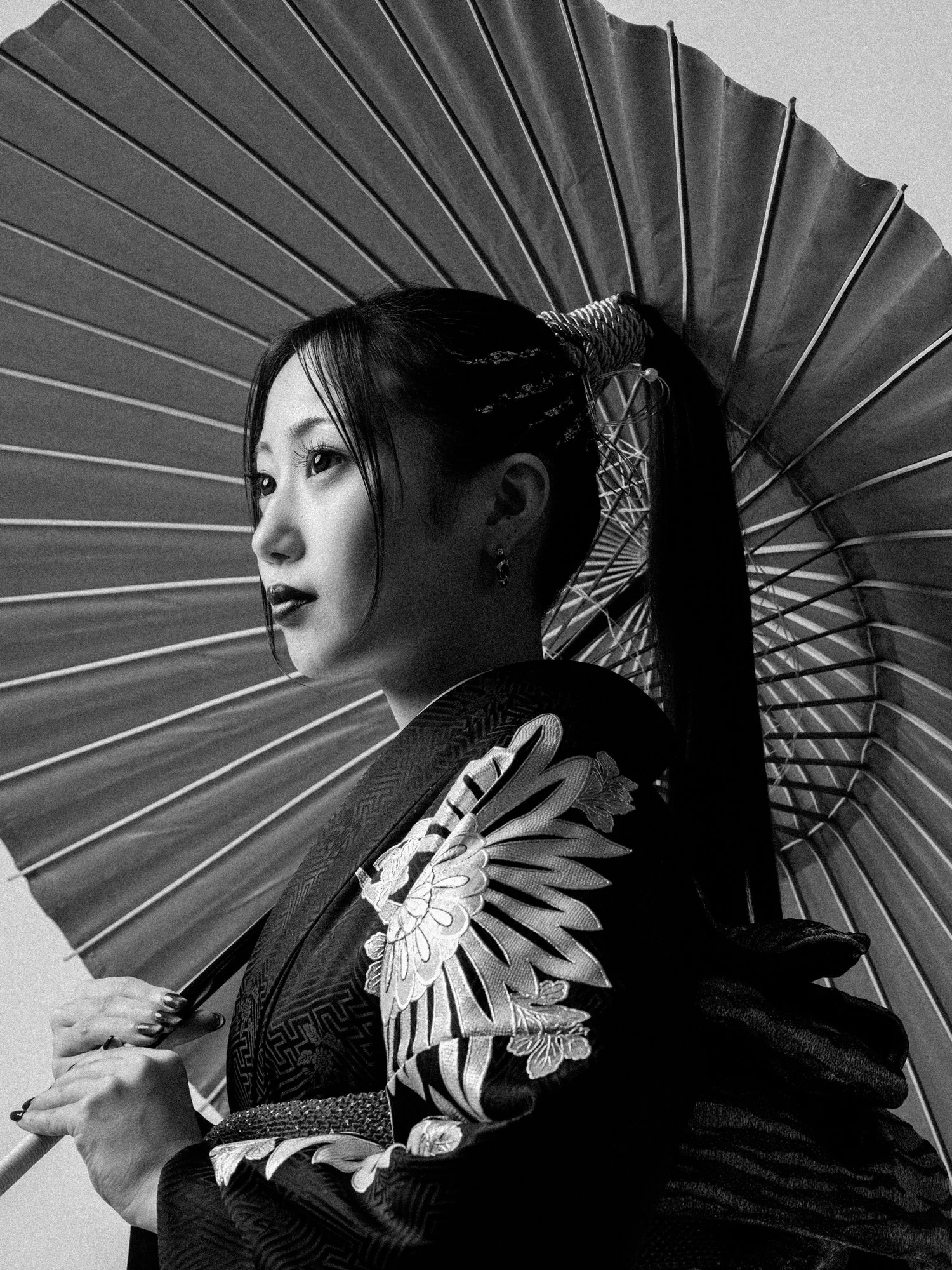 伝統的な着物を着た女性が和傘を持ち、ポーズをとっている黒と白の写真。