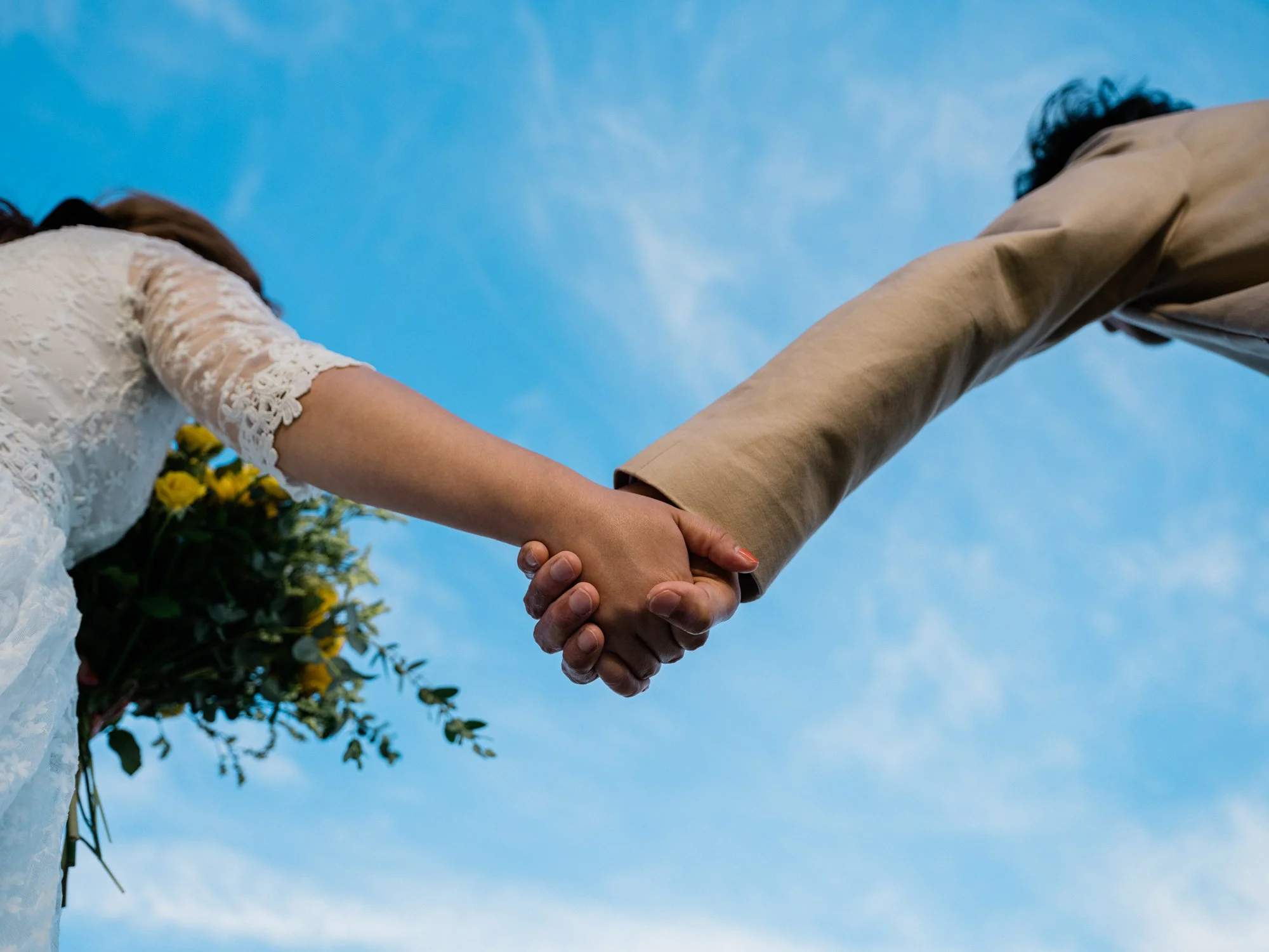 青空の下で手を取り合う男女の結婚式のカップル