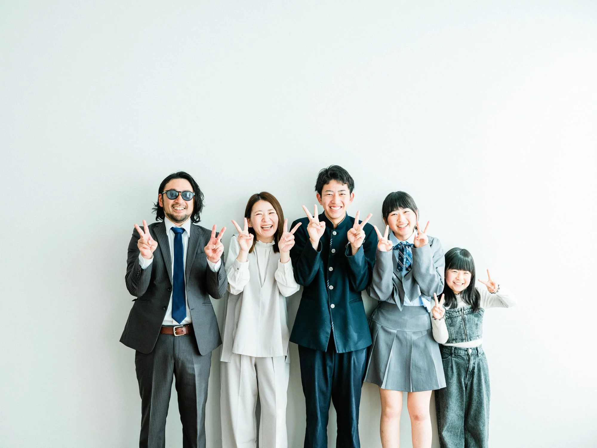 笑顔の家族が手でピースサインをしながらポーズをとっている。