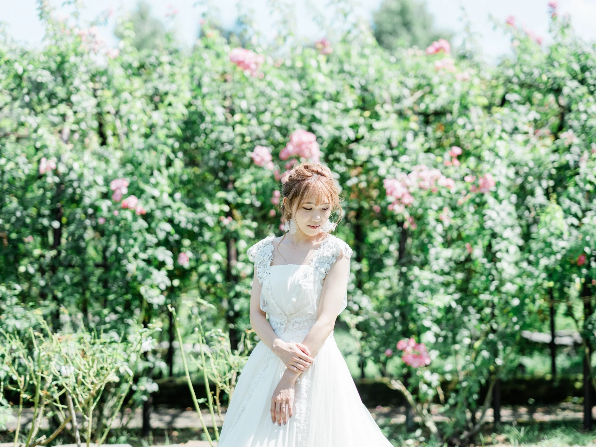 花に囲まれた屋外で白いドレスを着た若い女性が佇んでいる様子。