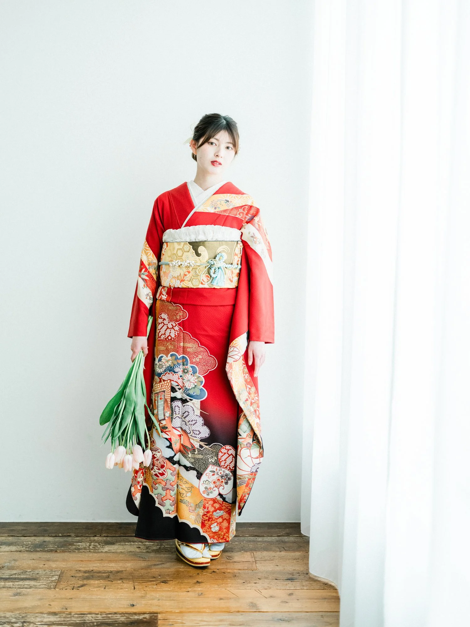 着物を着た女性がブーケの花束を持ちながら立っている成人式の写真。背景は白い壁と木製の床。
