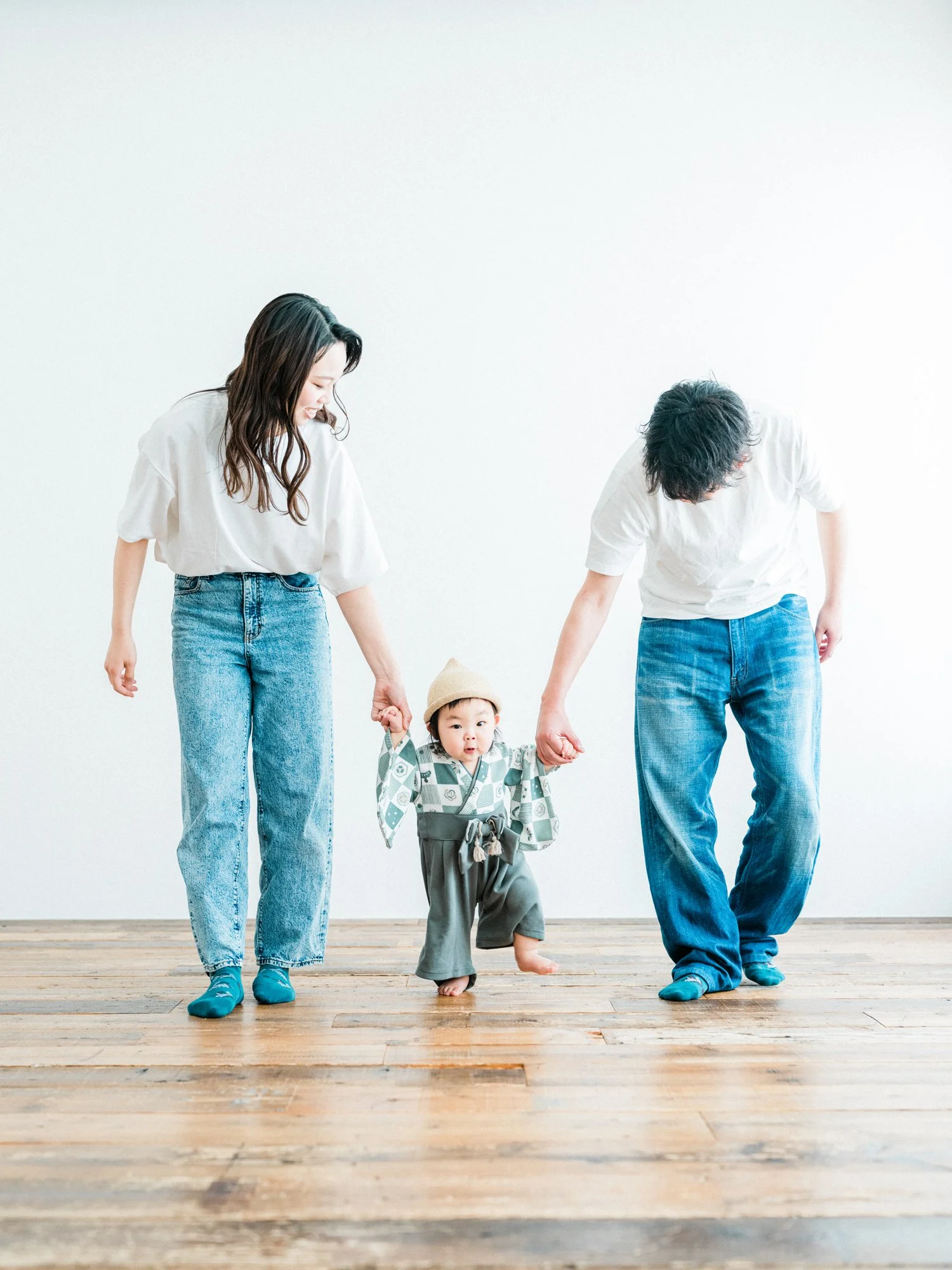 両親と子供が木製の床の上で手をつないで歩いている。