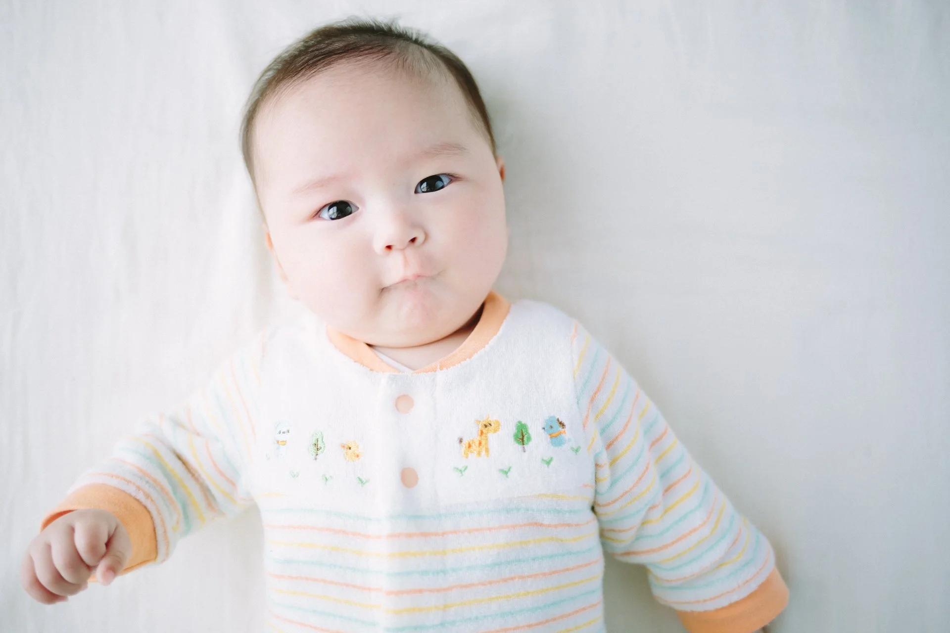 白い背景の前にいる幼い女の子が、寝転んでこちらを見ている。
