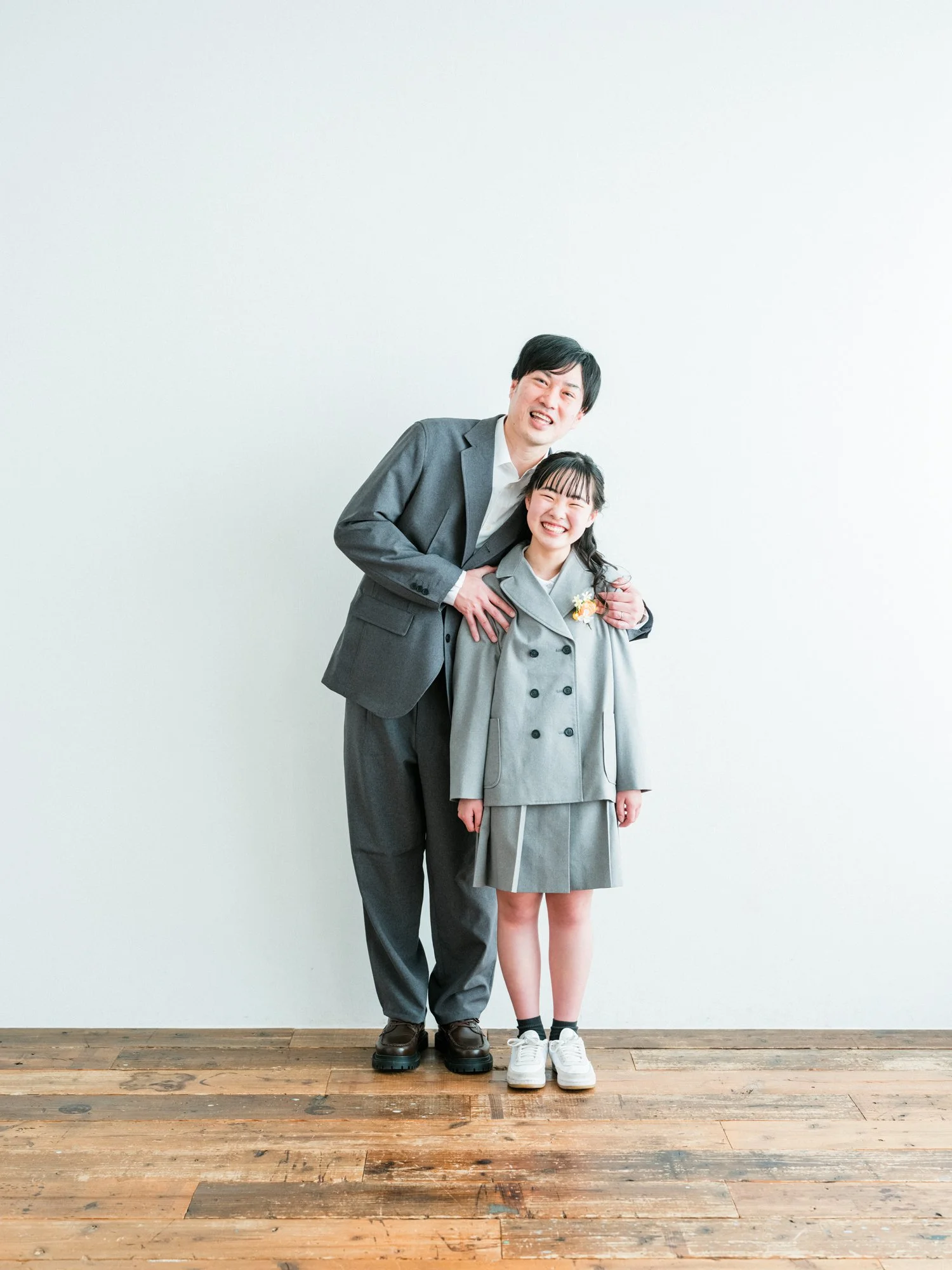 スーツを着た父親と制服を着た若い小学が笑顔で並んでいる。卒業式の写真。