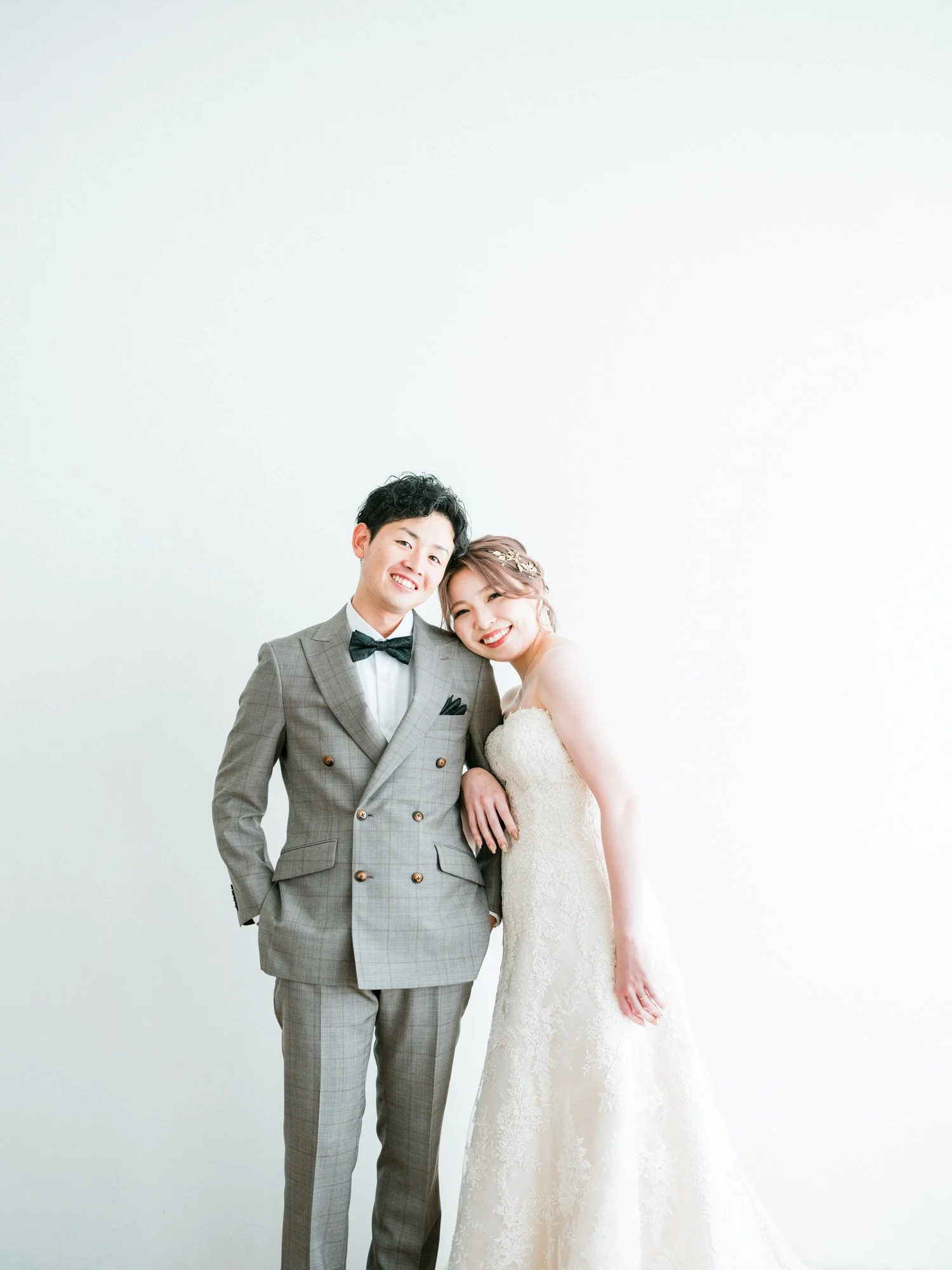 結婚式を挙げたカップルの写真。男性はグレーのスーツと蝶ネクタイ、女性は白いレースのドレスを着ている。二人とも笑顔。