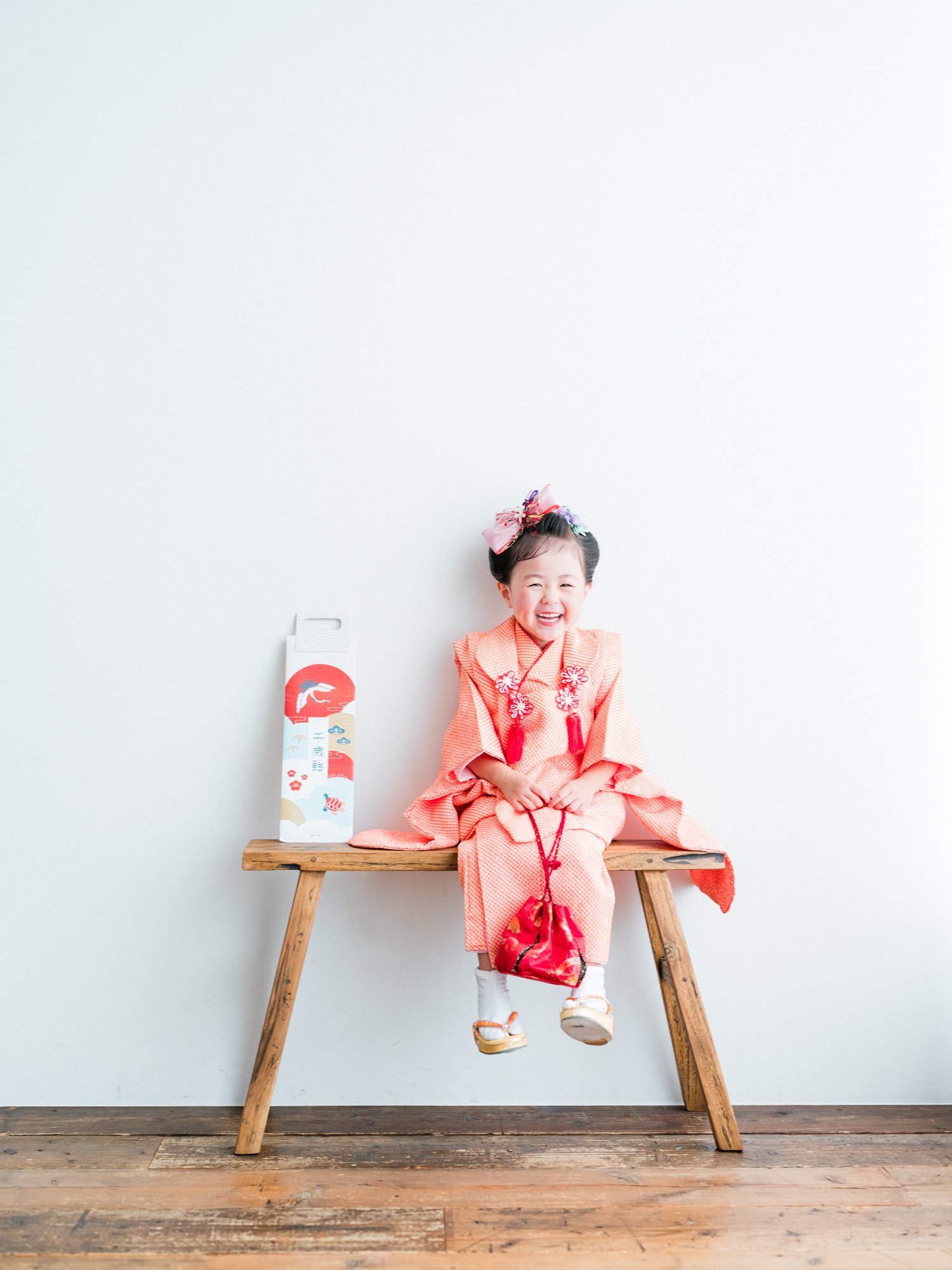 笑顔の女の子が伝統的な七五三の着物を着て、木製の長椅子に座っている。