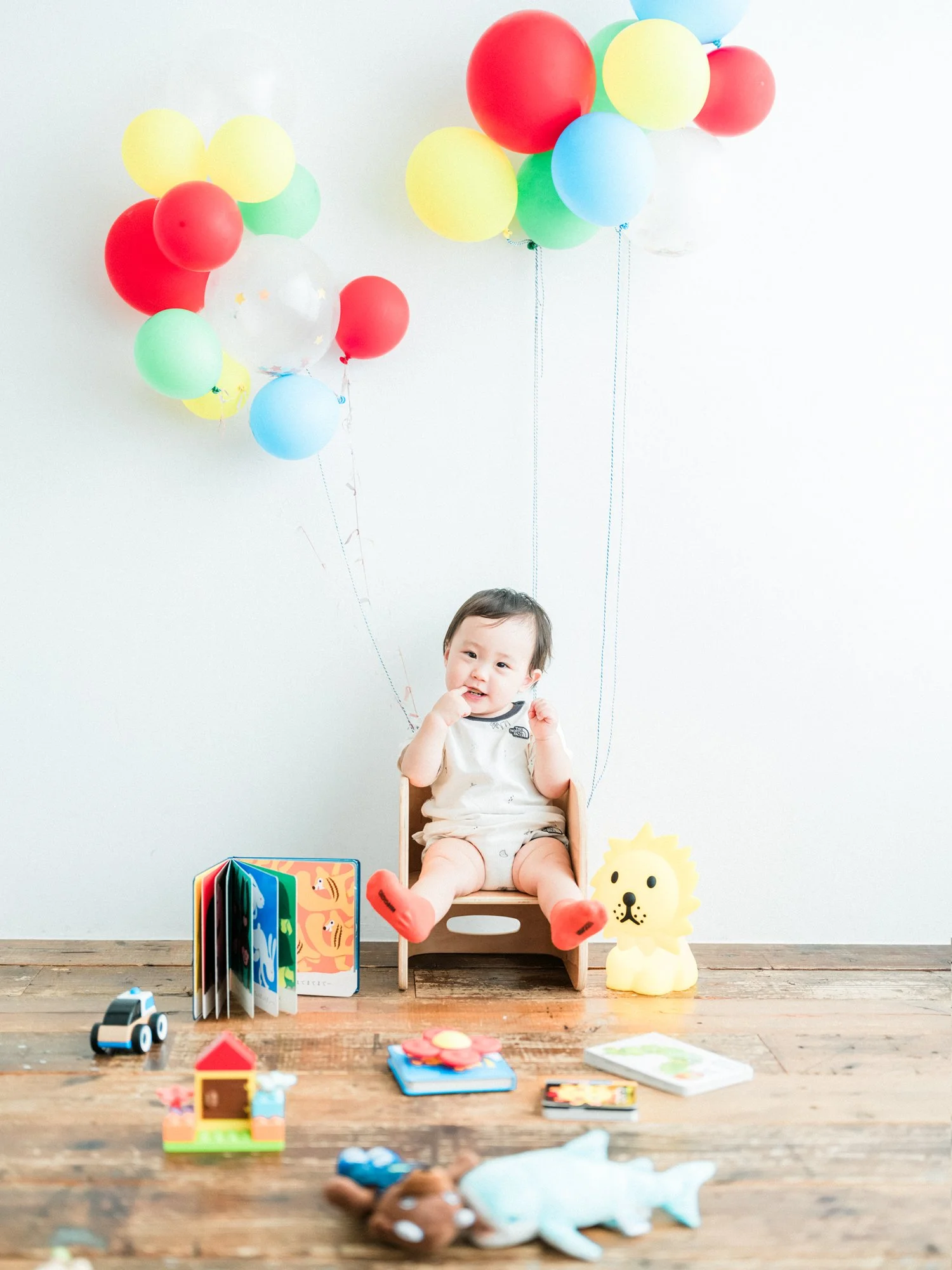 子供が木製の椅子に座っており、背景にバルーンや絵本、おもちゃが置かれている。