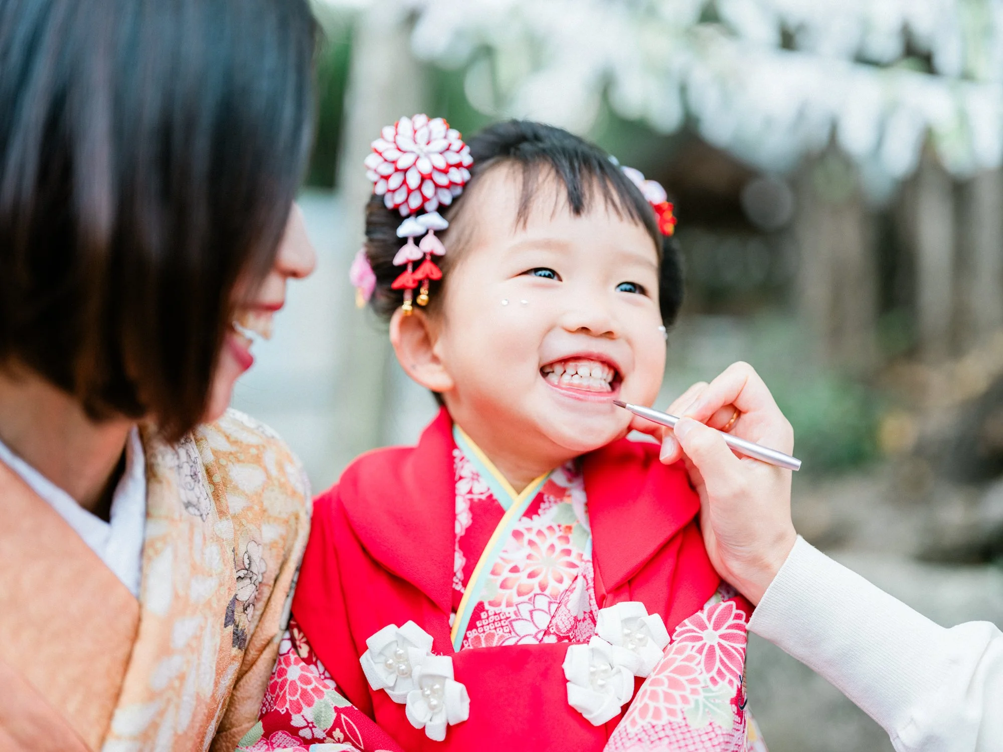 女性と子供が笑顔で着物を着ている。子供は髪飾りをつけ、白い花の飾りとともに晴れやかな表情を見せている。