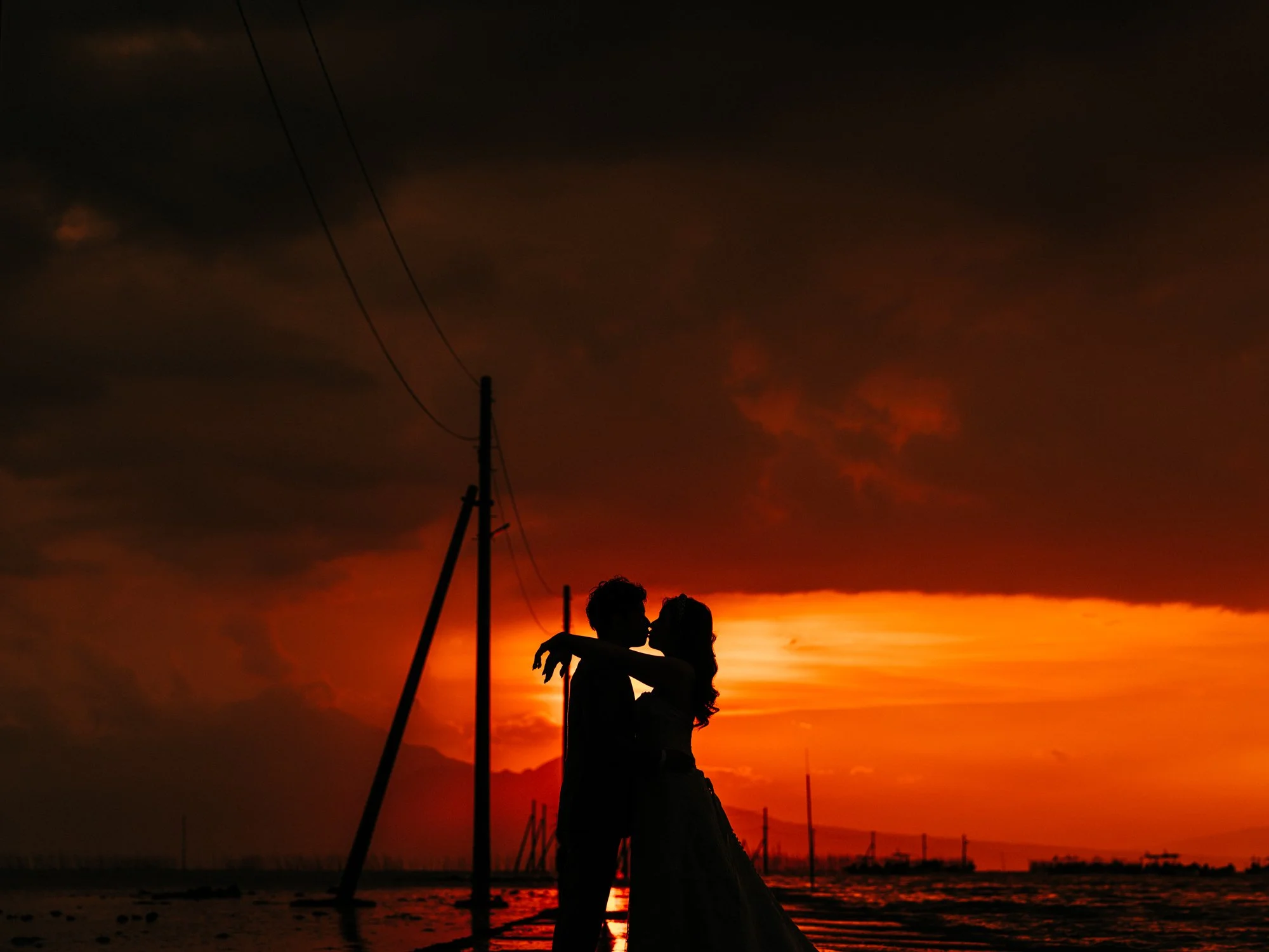 夕焼けの空の背景に、二人の人物が抱き合っているシルエットのウェディング写真。