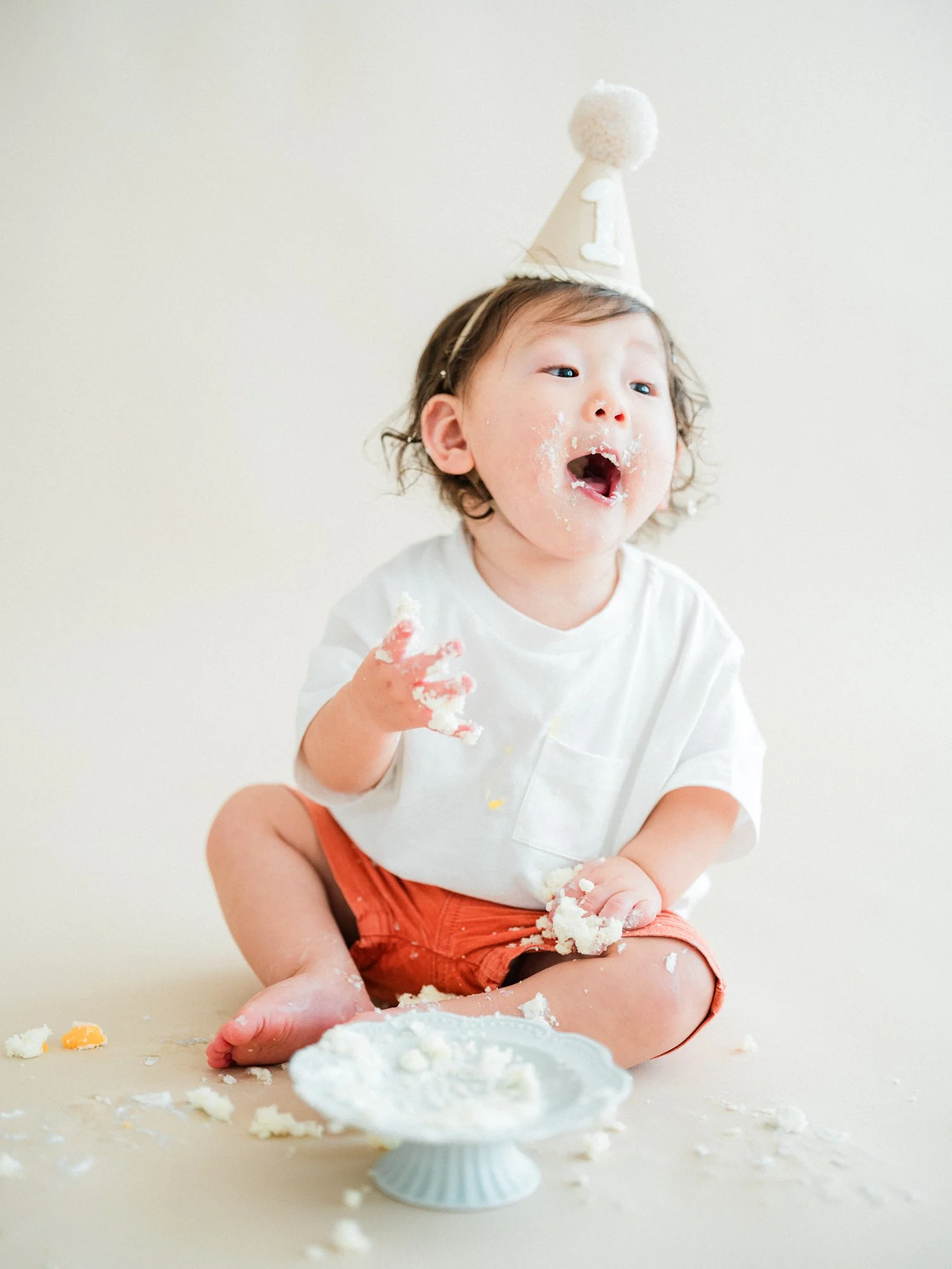 誕生日パーティーの帽子をかぶった子供がスマッシュケーキを食べている様子。