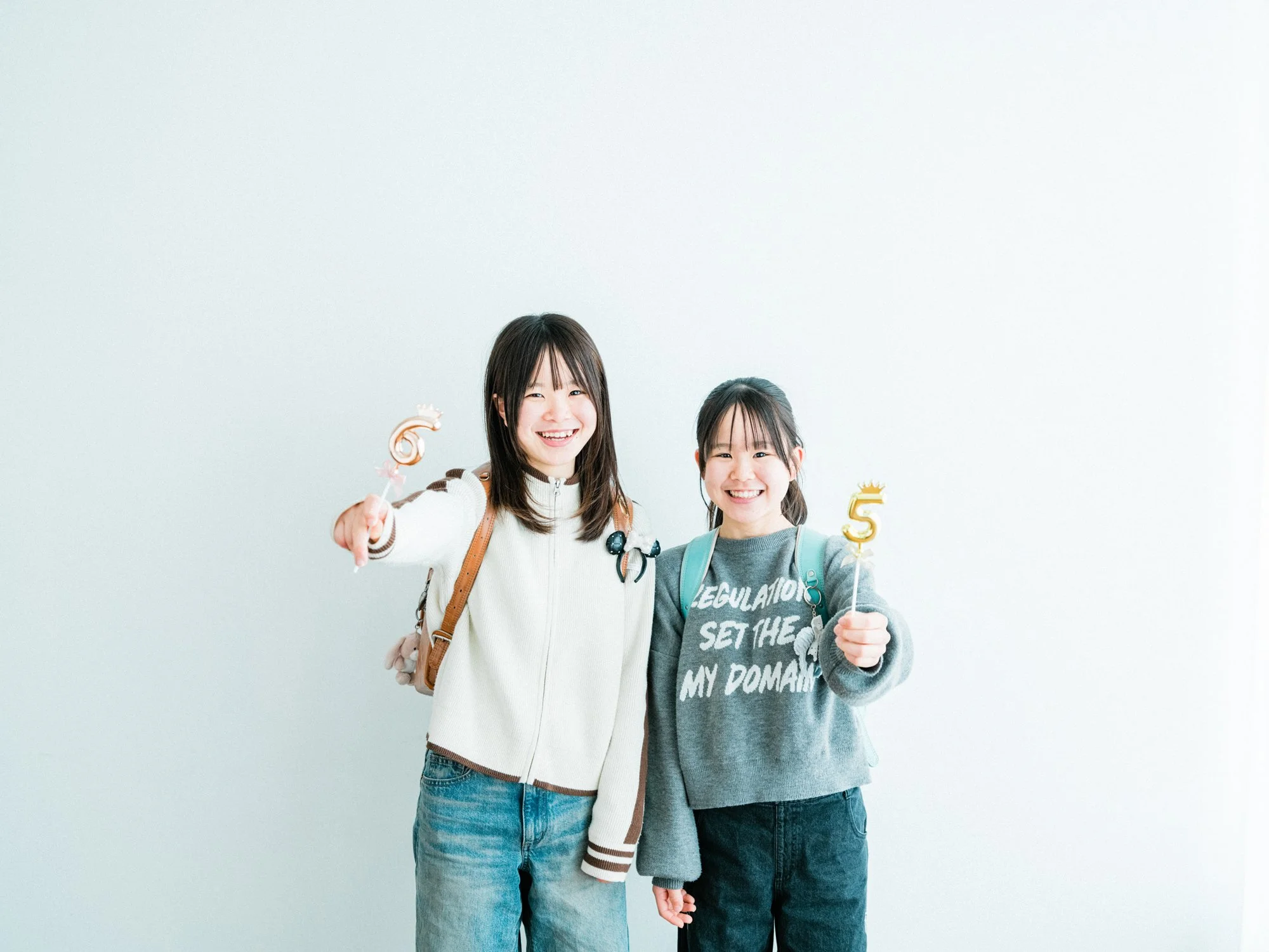 白い壁の前で笑顔の二人の小学生が手を挙げている。