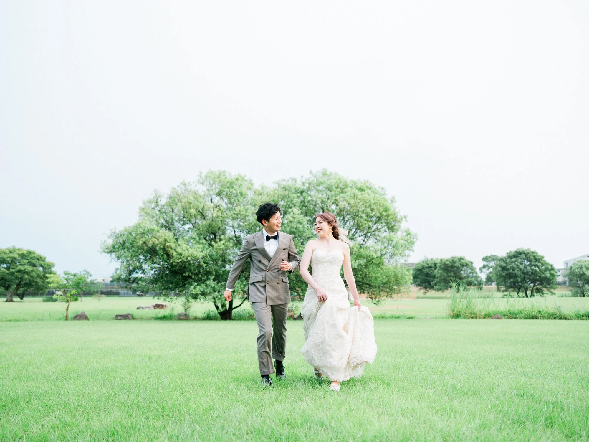 緑の公園で結婚式を挙げている新郎新婦が歩いている様子。背景には木々が広がっている。