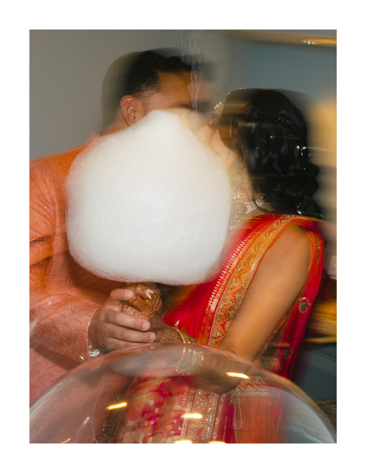 A couple dressed in traditional Indian attire, sharing a tender moment during a celebration, with a cotton candy in the foreground.