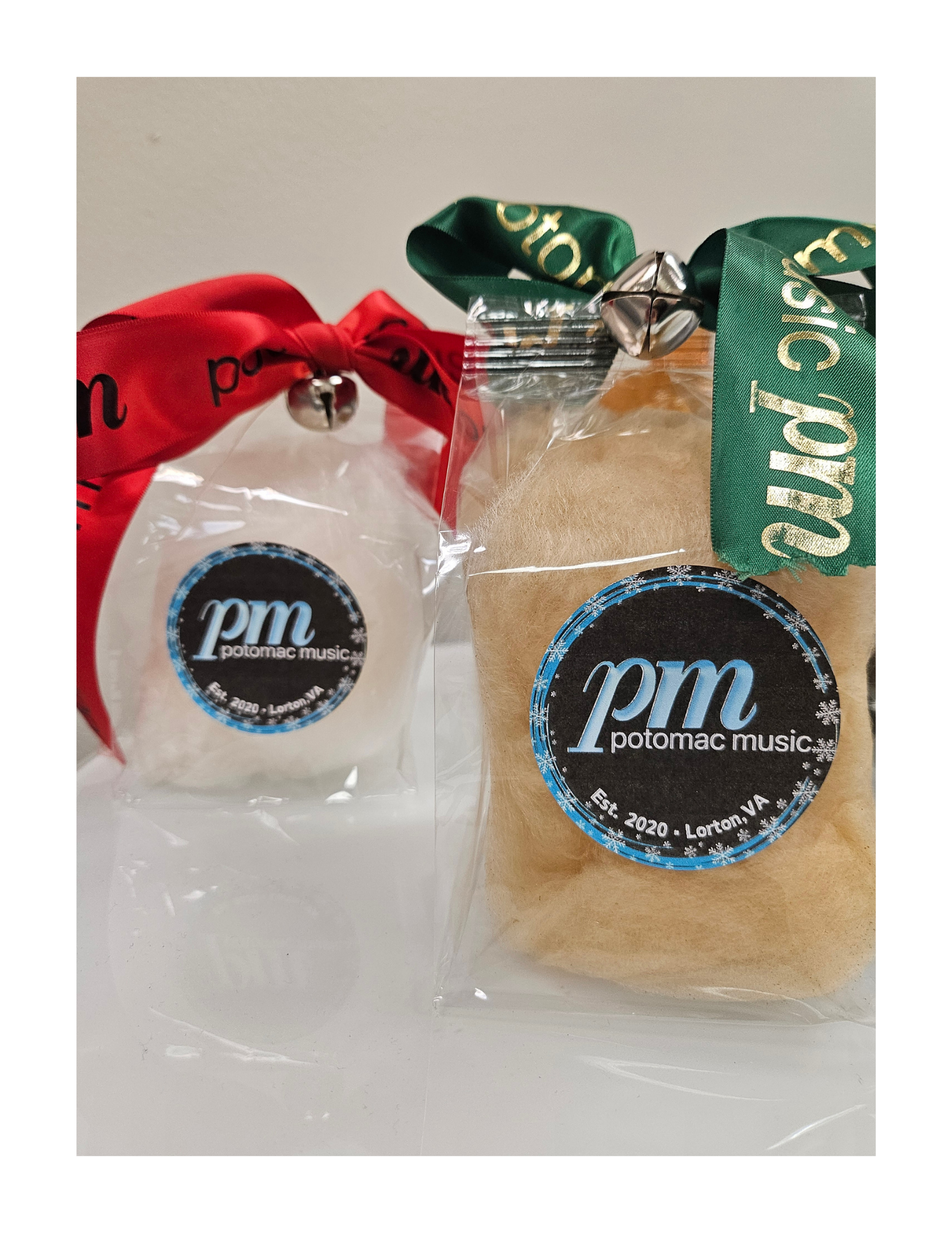 Two holiday, dye-free cotton candy gift bags with Potomac Music LLC of Lorton, VA logos, one with red ribbon and jingle bell, the other with green ribbon, placed on a white surface.