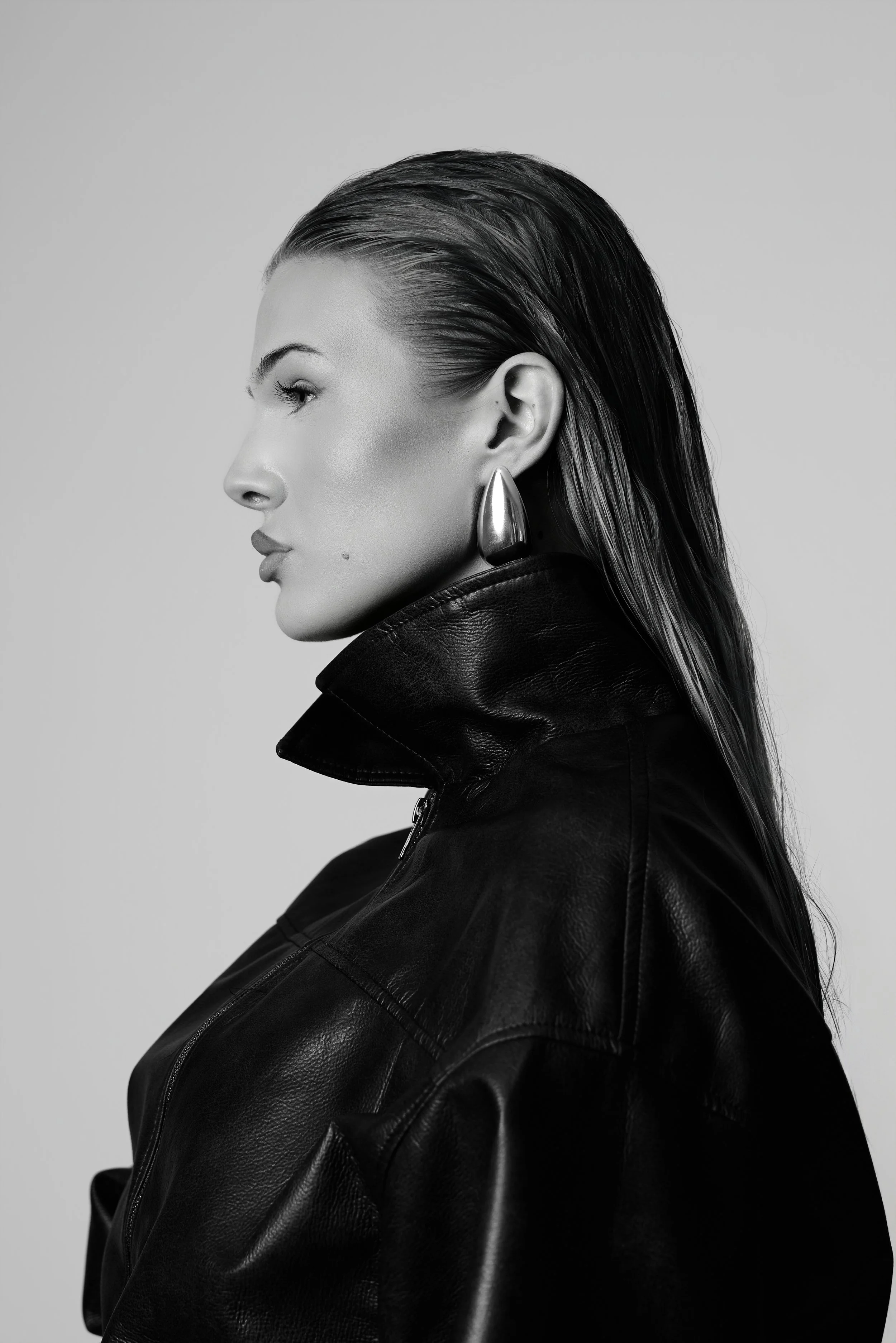 Black and white portrait of a woman in profile with wet hairstyle, wearing a leather jacket and a large metallic earring.