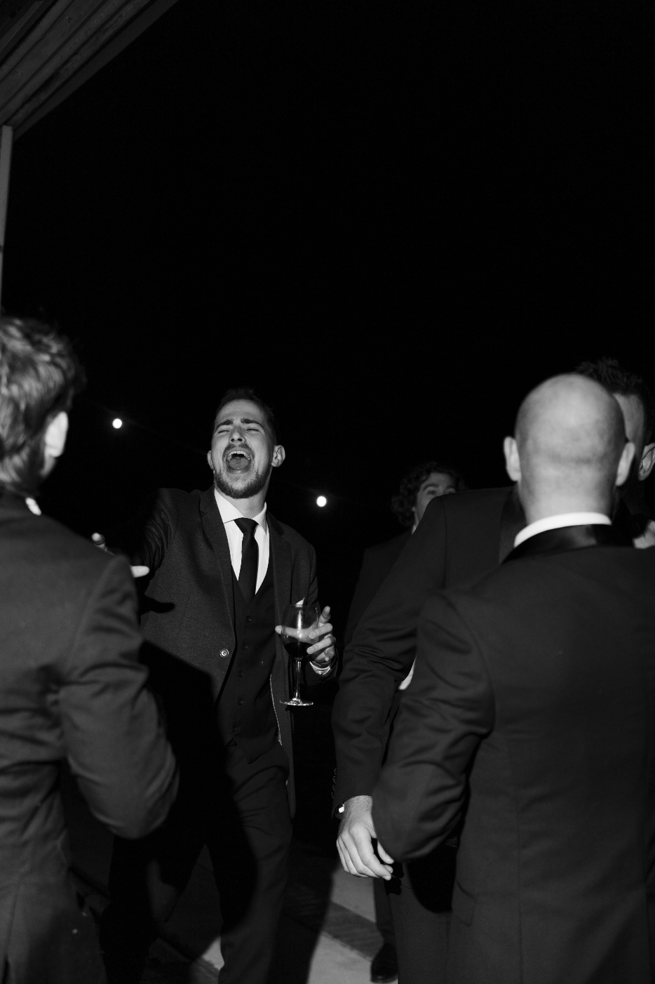 A group of men in formal suits having a conversation and laughing at night.